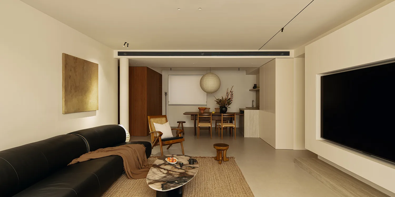 Cozy living room with wooden furniture, a rug, and a well-lit atmosphere, visible kitchen in the background
