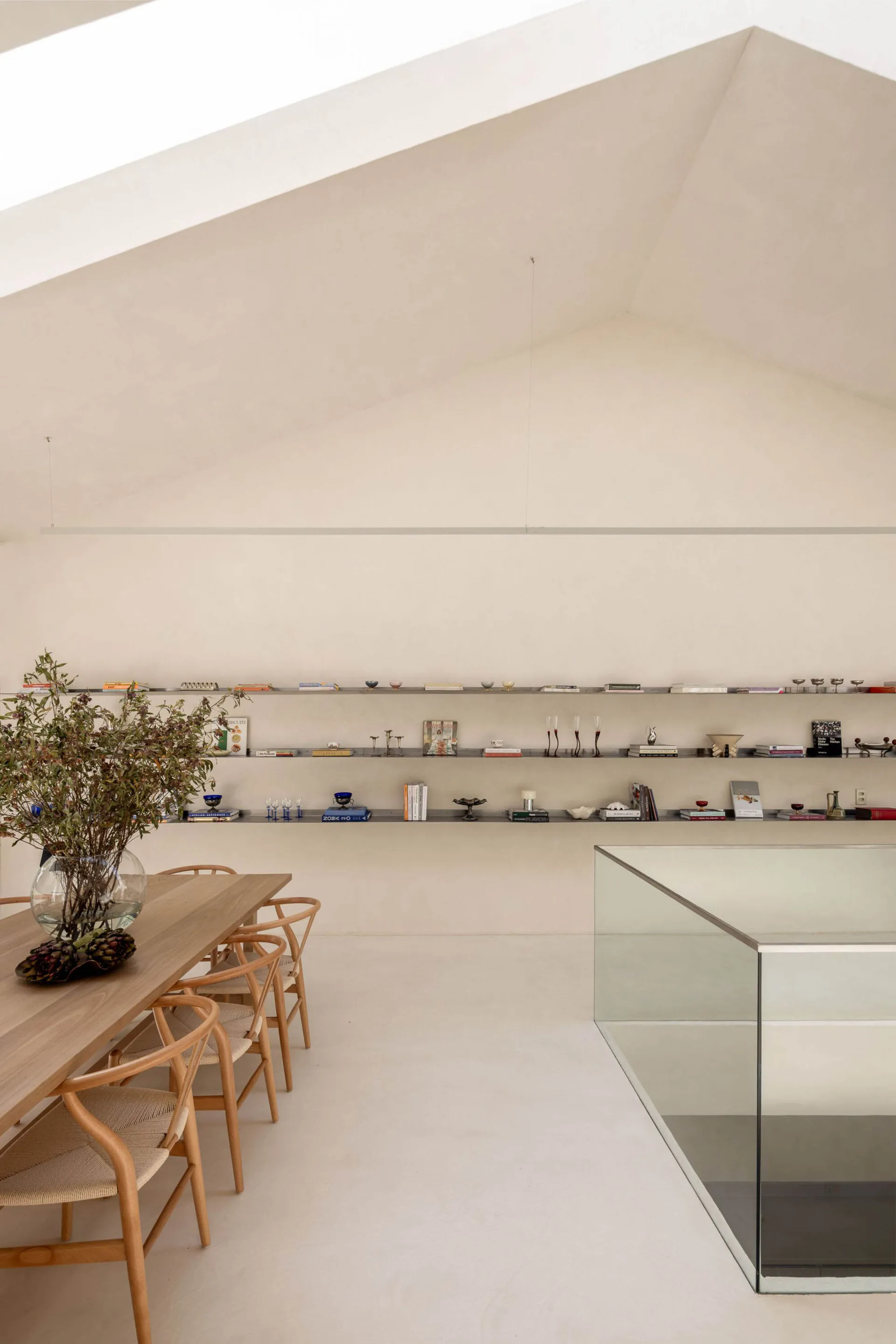 A modern living room with a glass countertop, dining table, bookshelf, and potted plant, featuring a white color scheme and natural lighting