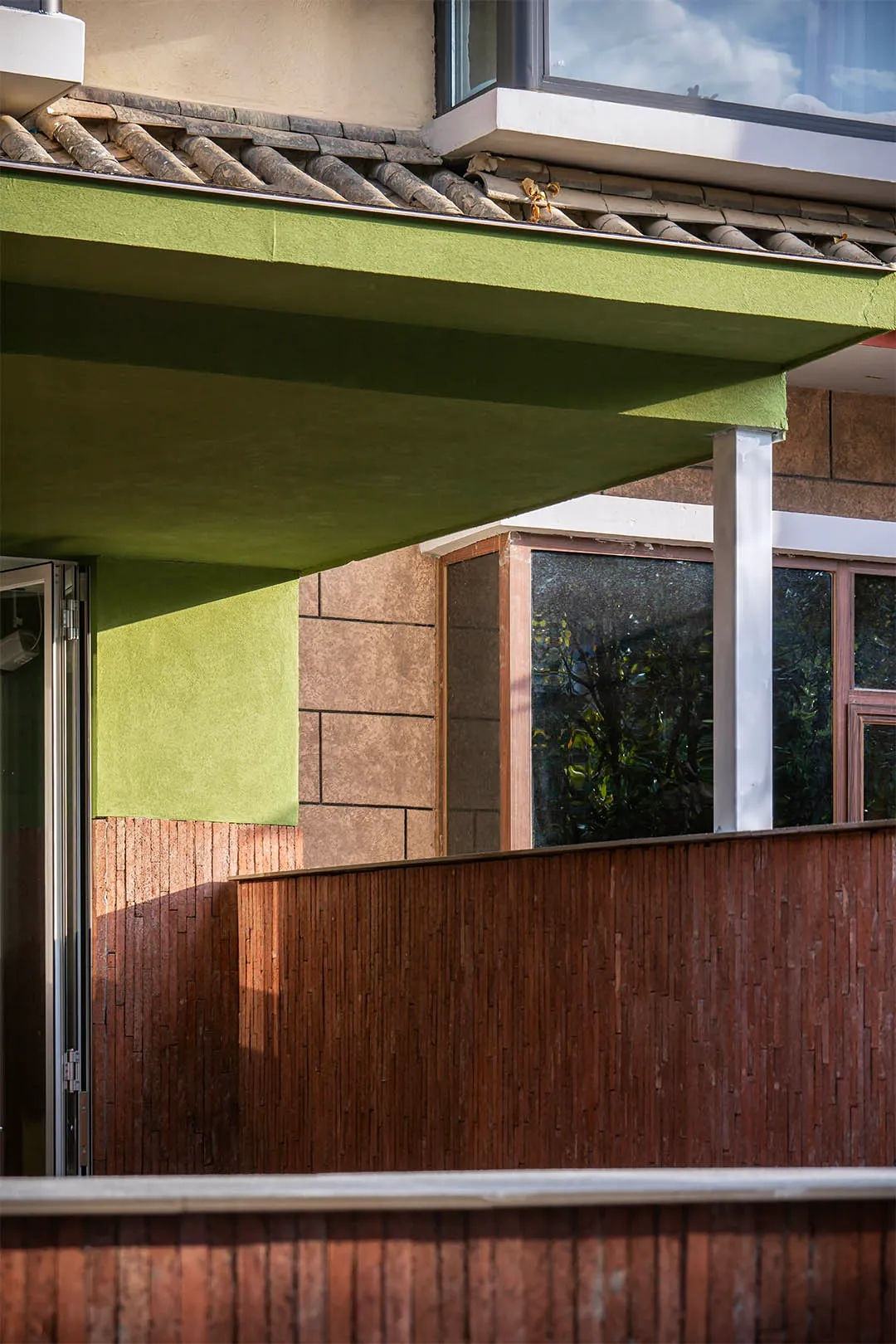A modern house with a green roof, wooden fence, and large window, set against a bright and warm background