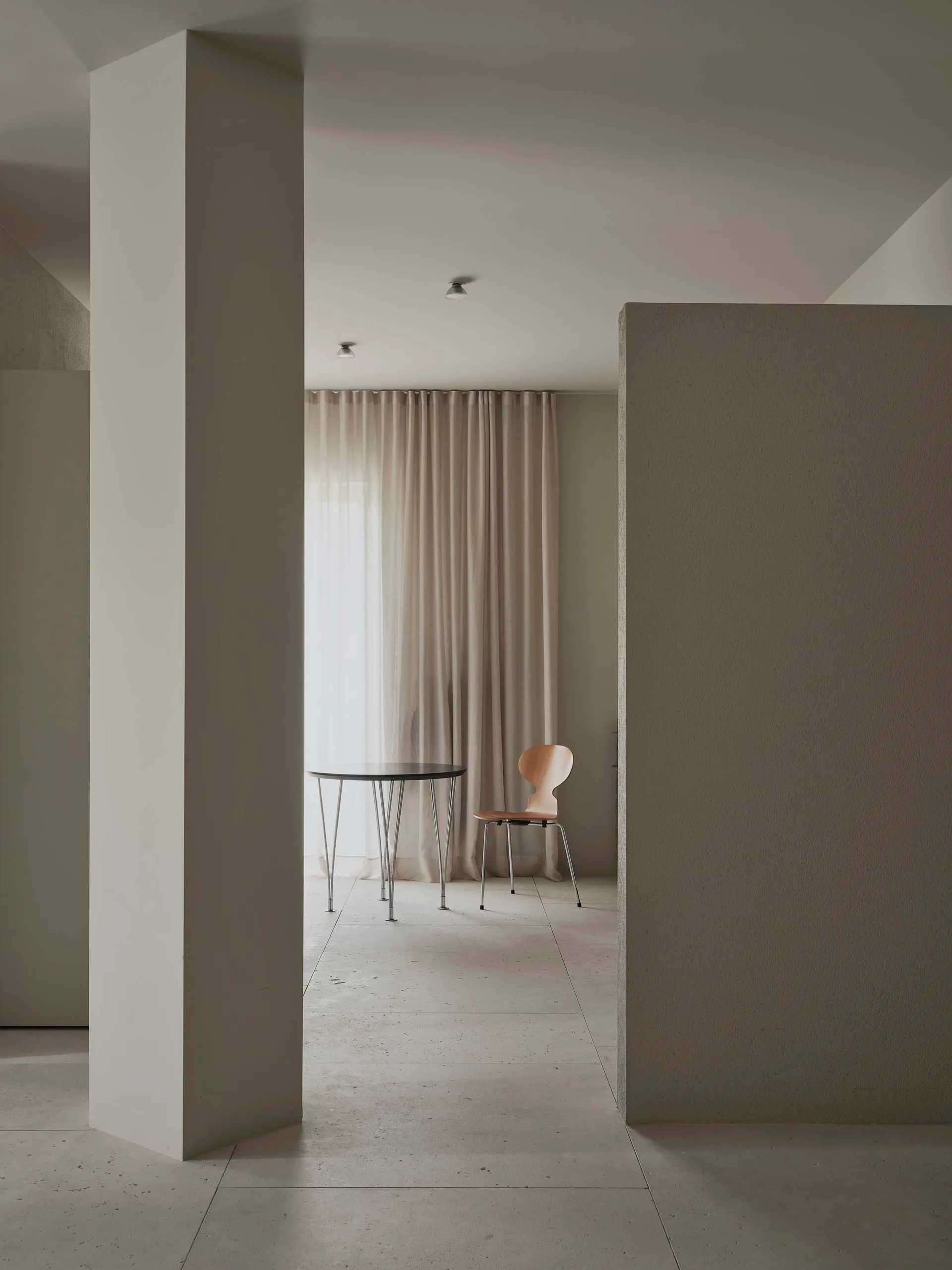 A modern dining room with a white table and chairs, surrounded by white walls and a window, with a minimalist and elegant atmosphere