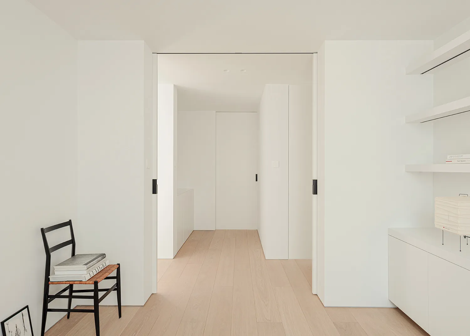 A bright and welcoming hallway with a white color scheme, wood accents, and a chair in the corner, set against a modern and clean backdrop