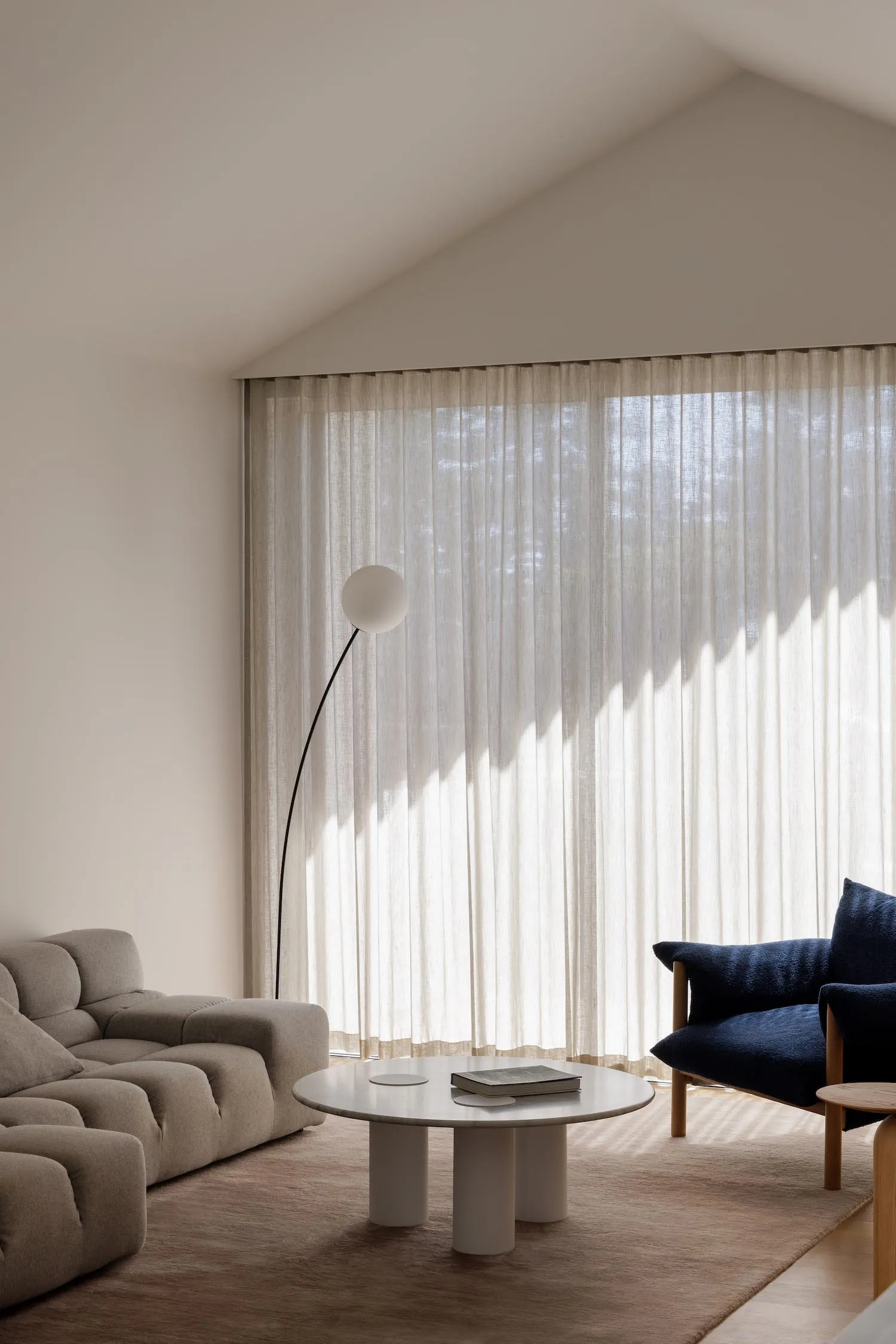 Cozy living room with a white couch, chair, and dining table, decorated with white curtains and a lamp, creating a warm and inviting atmosphere