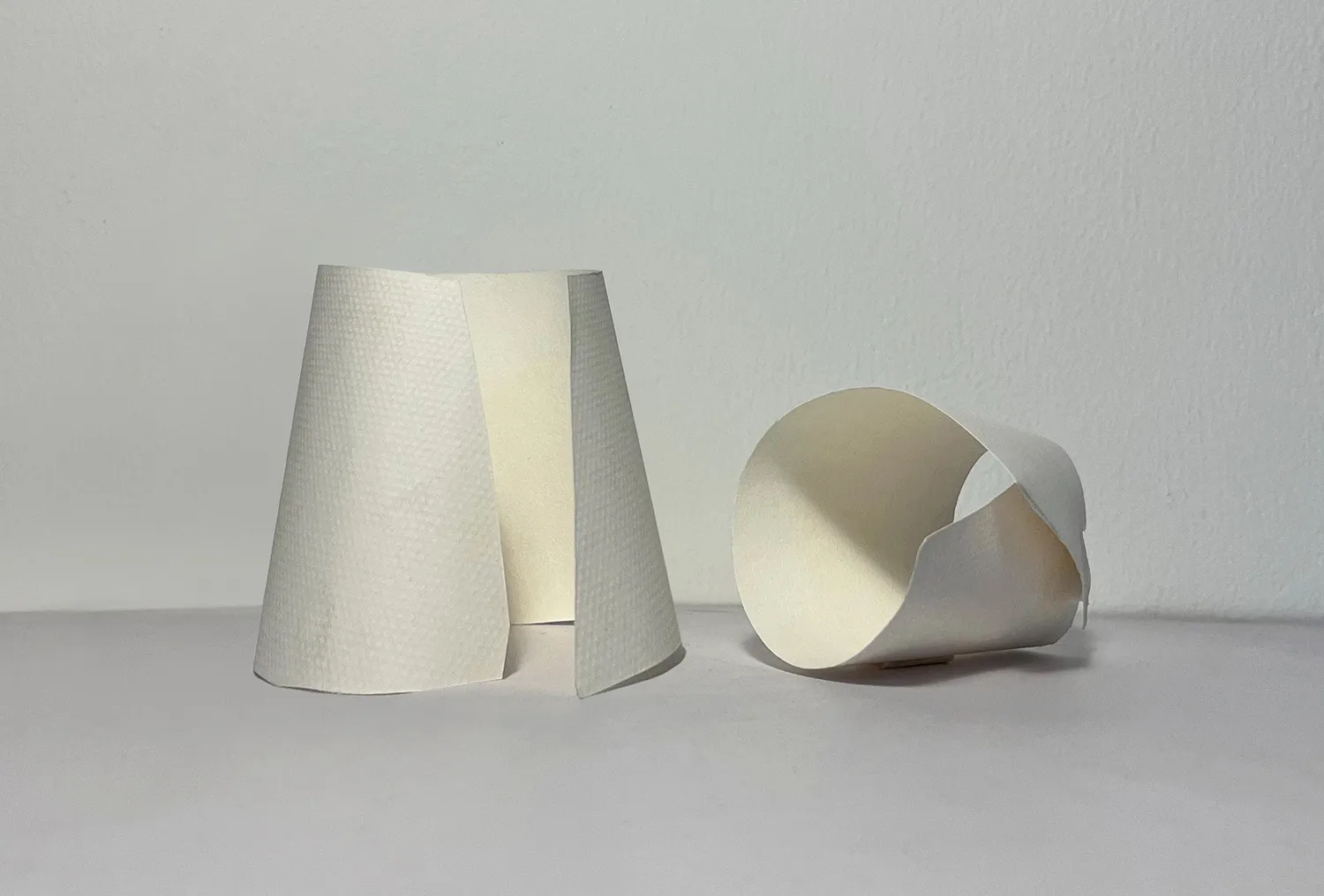 A minimalist room with three white objects stacked on a table against a white wall