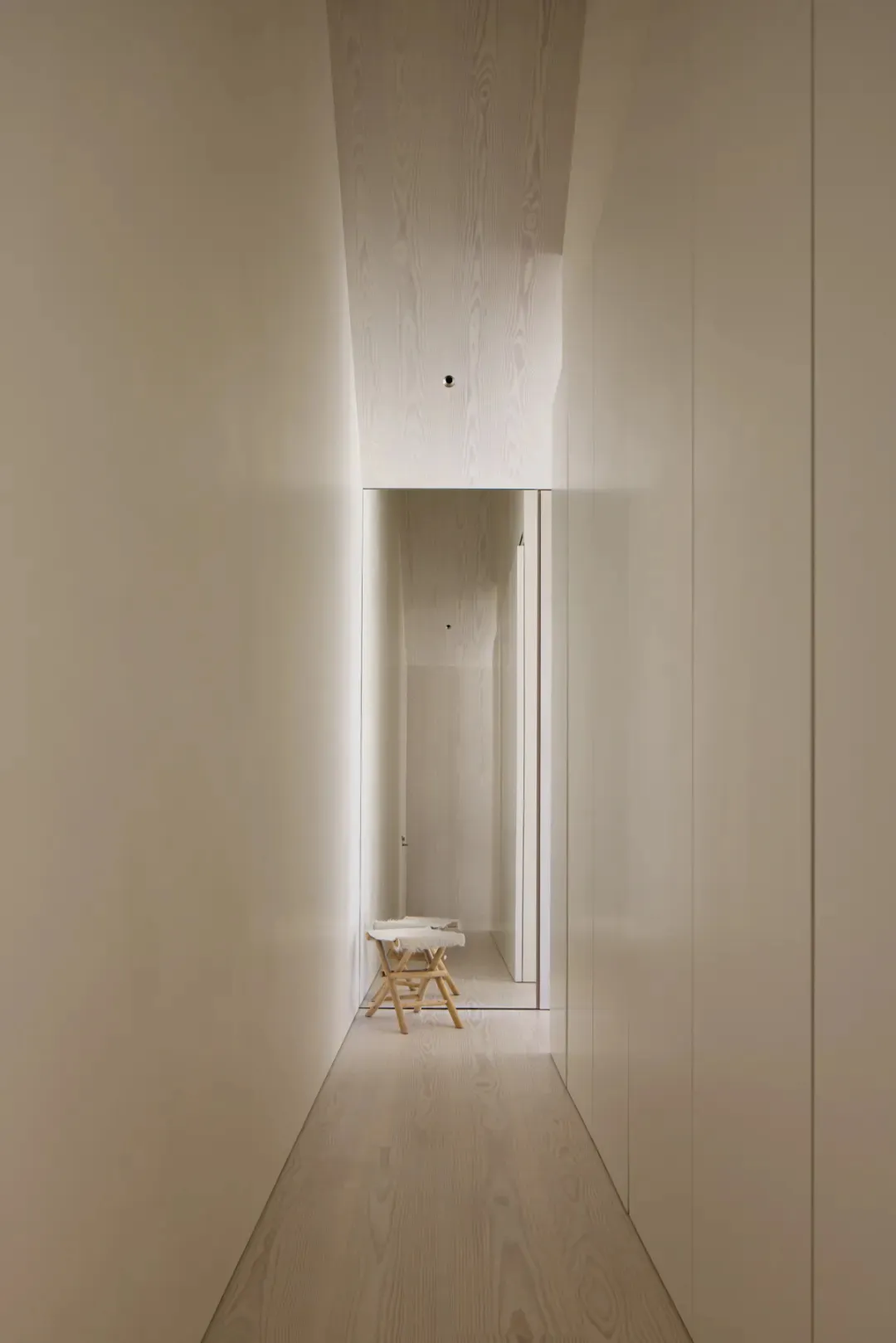 Narrow hallway with a white color scheme, a small table, and a chair, creating a cozy atmosphere with dim lighting