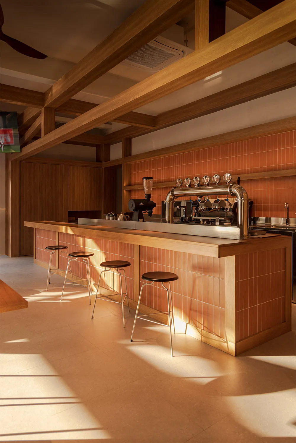 A well-lit bar area with a wooden counter, black stools, and a coffee machine in a restaurant setting, featuring natural lighting and high-quality materials