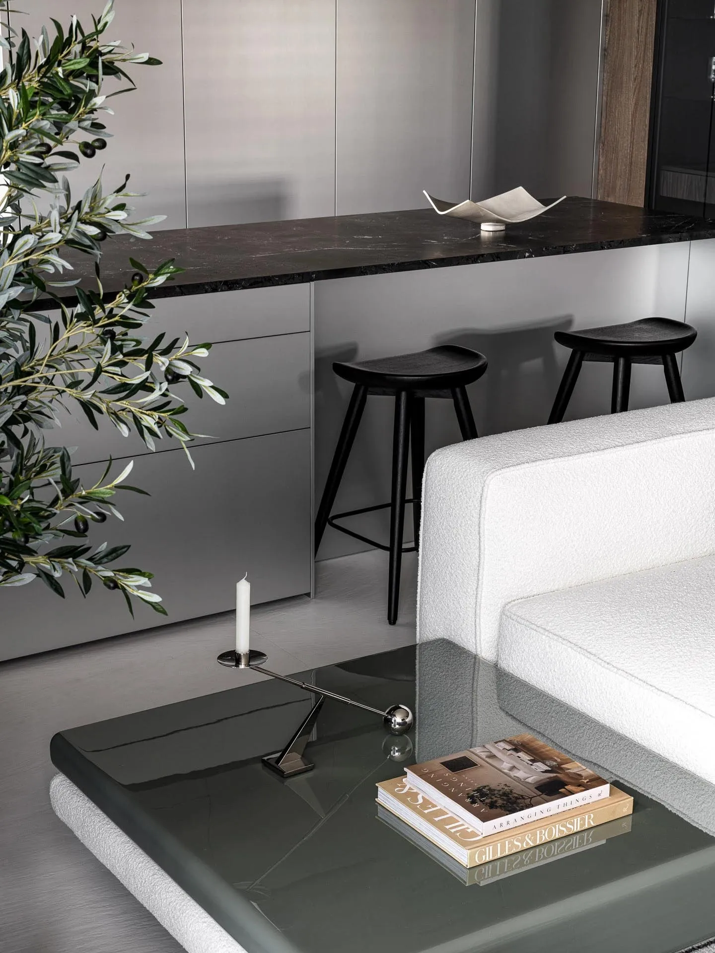 Modern living room with a white couch, glass coffee table, marble countertop, and black and white theme, featuring three black stools and a potted plant