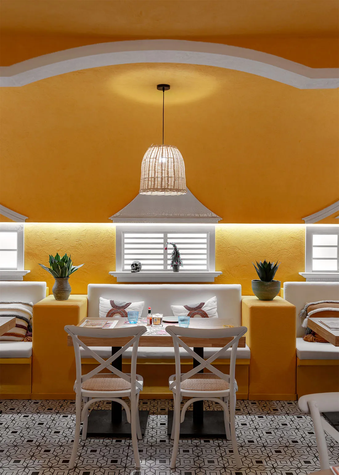 A cozy restaurant with a yellow color scheme, featuring a table with white chairs and potted plants, creating a warm and inviting atmosphere