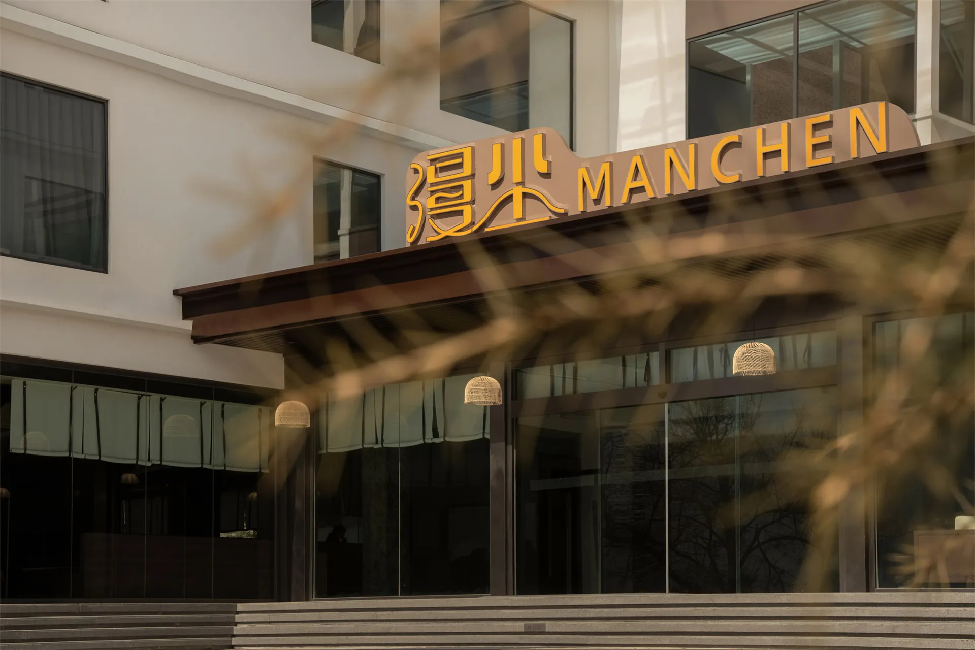 A modern hotel building with a glass front and black frame, set against a foreign language sign, shot from a low angle with soft and diffused lighting