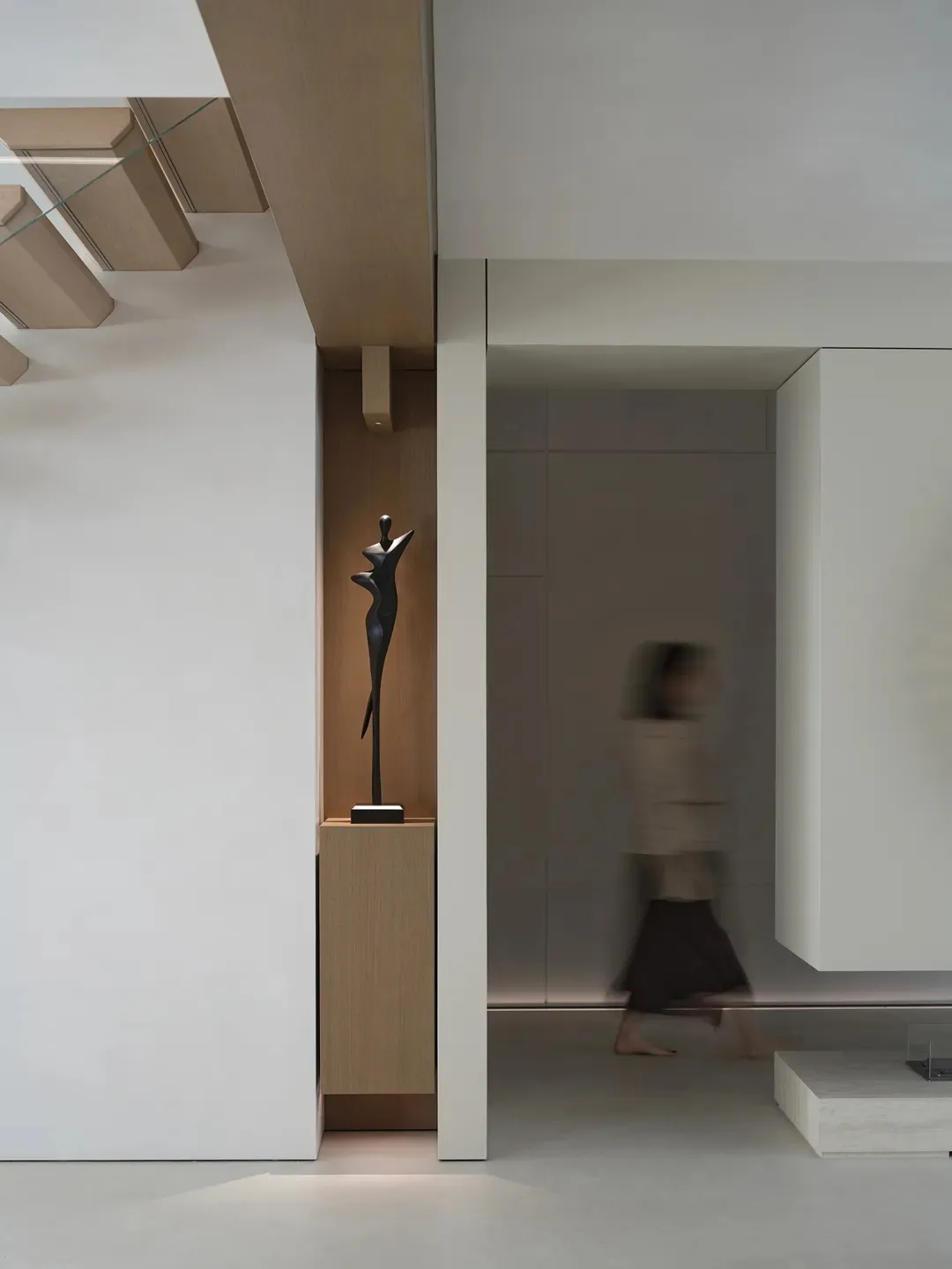 A woman in a brown coat walks down a calm and quiet hallway with wooden walls and floor