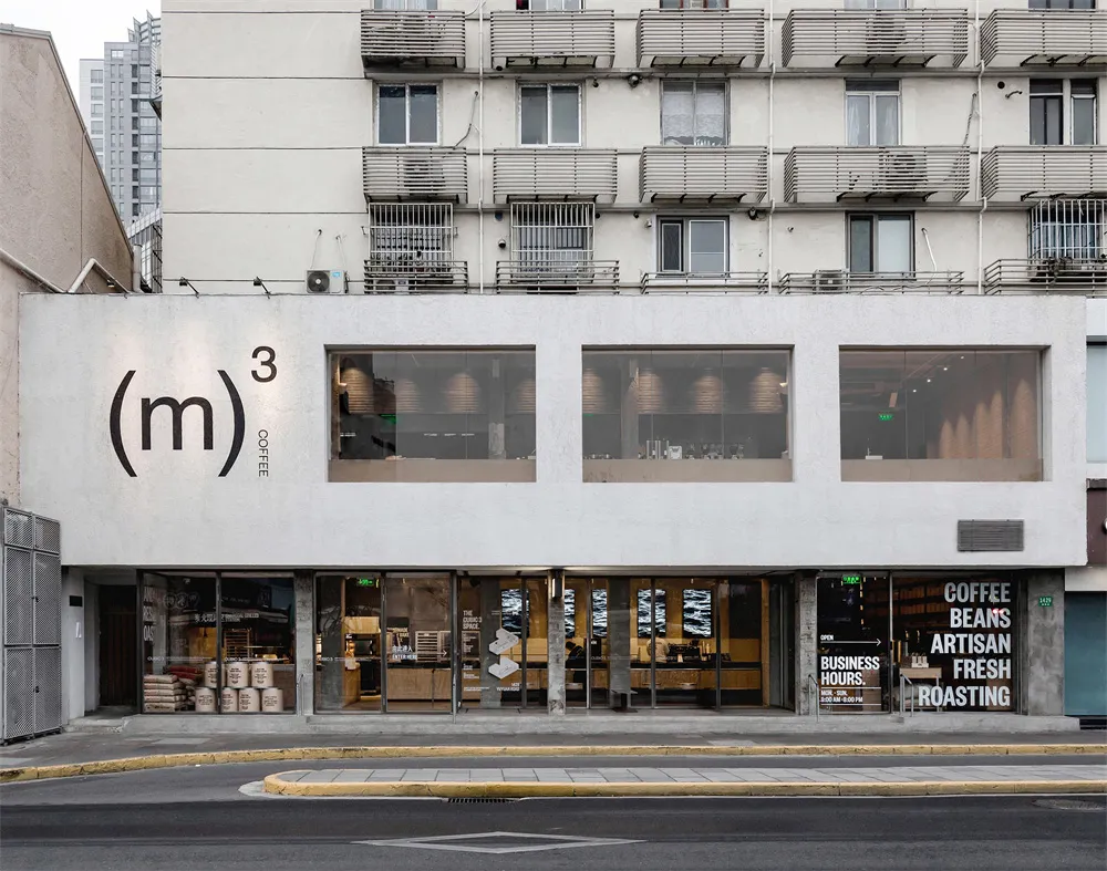 A modern commercial building with a white concrete facade, a large metal-framed window, and natural light streaming in