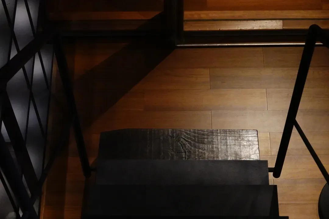 A dimly lit, vintage staircase with dark wooden treads and a wooden floor, set against a neutral background