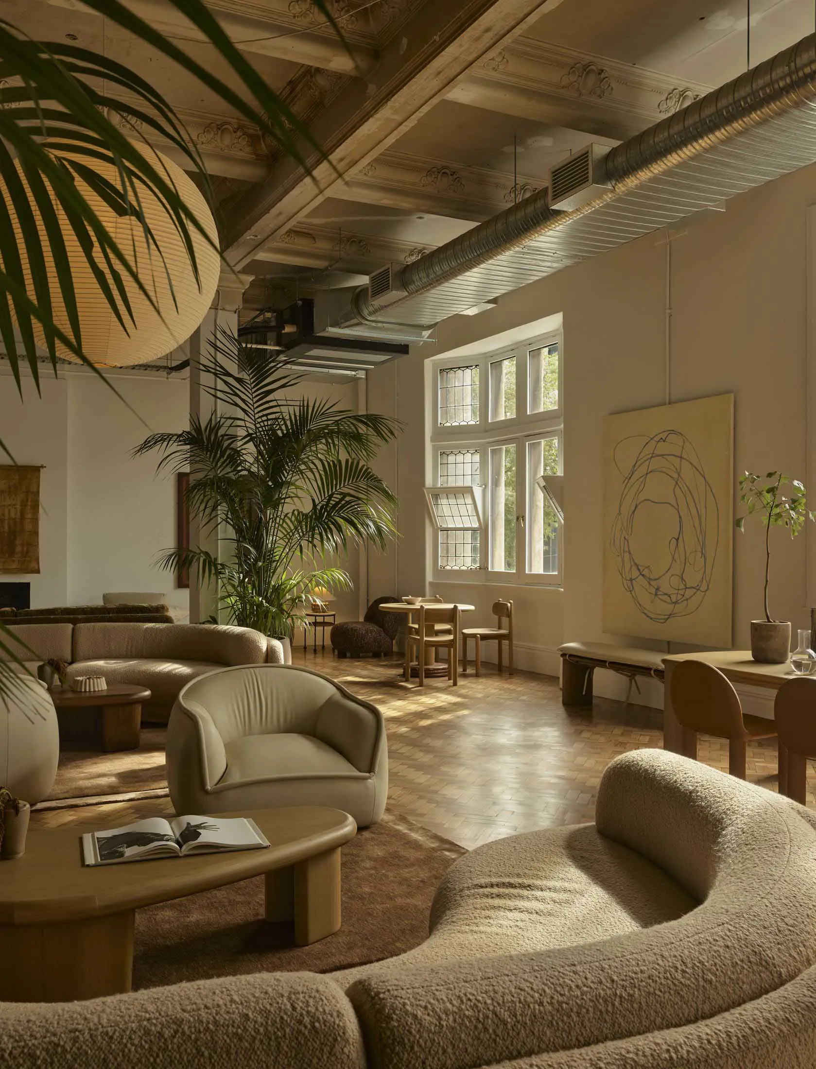 Bright and welcoming open living space with natural light, wood, glass, and metal materials, featuring a couch, chair, dining table, and potted plants