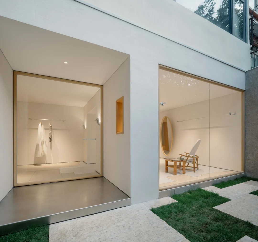 Bright and airy modern interior space with a white color scheme, a large mirror, and a chair in a corner, lit by natural light through a glass door