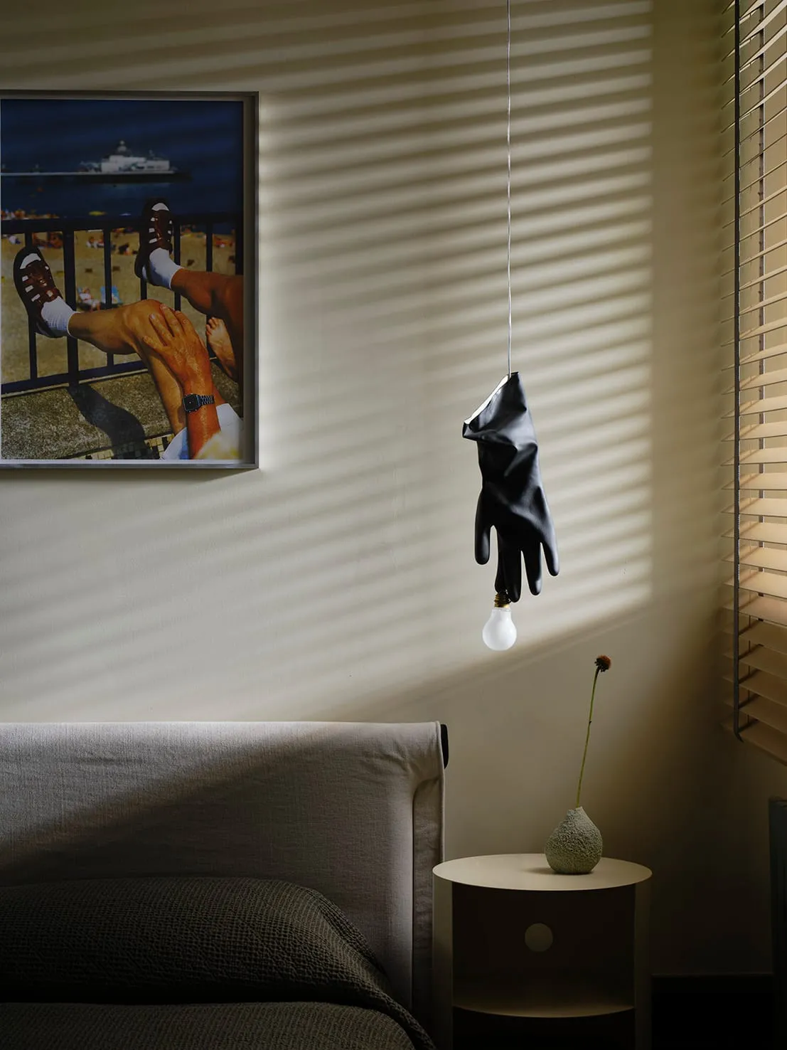 Cozy living room with a modern couch, a chair, a black glove hanging from the ceiling, and a painting on the wall, with dim lighting