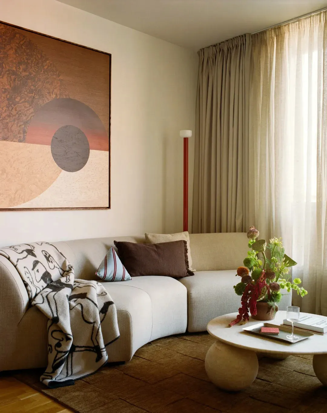 Cozy living room with a white couch, a red lamp, and natural light from the window, decorated with a vase and a potted plant