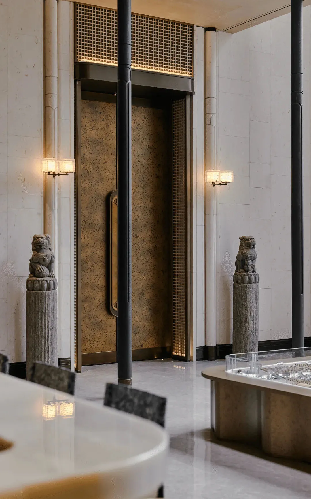 A well-lit, modern lobby with marble and stone surfaces, featuring a variety of furniture and sculptures, and a warm, inviting atmosphere