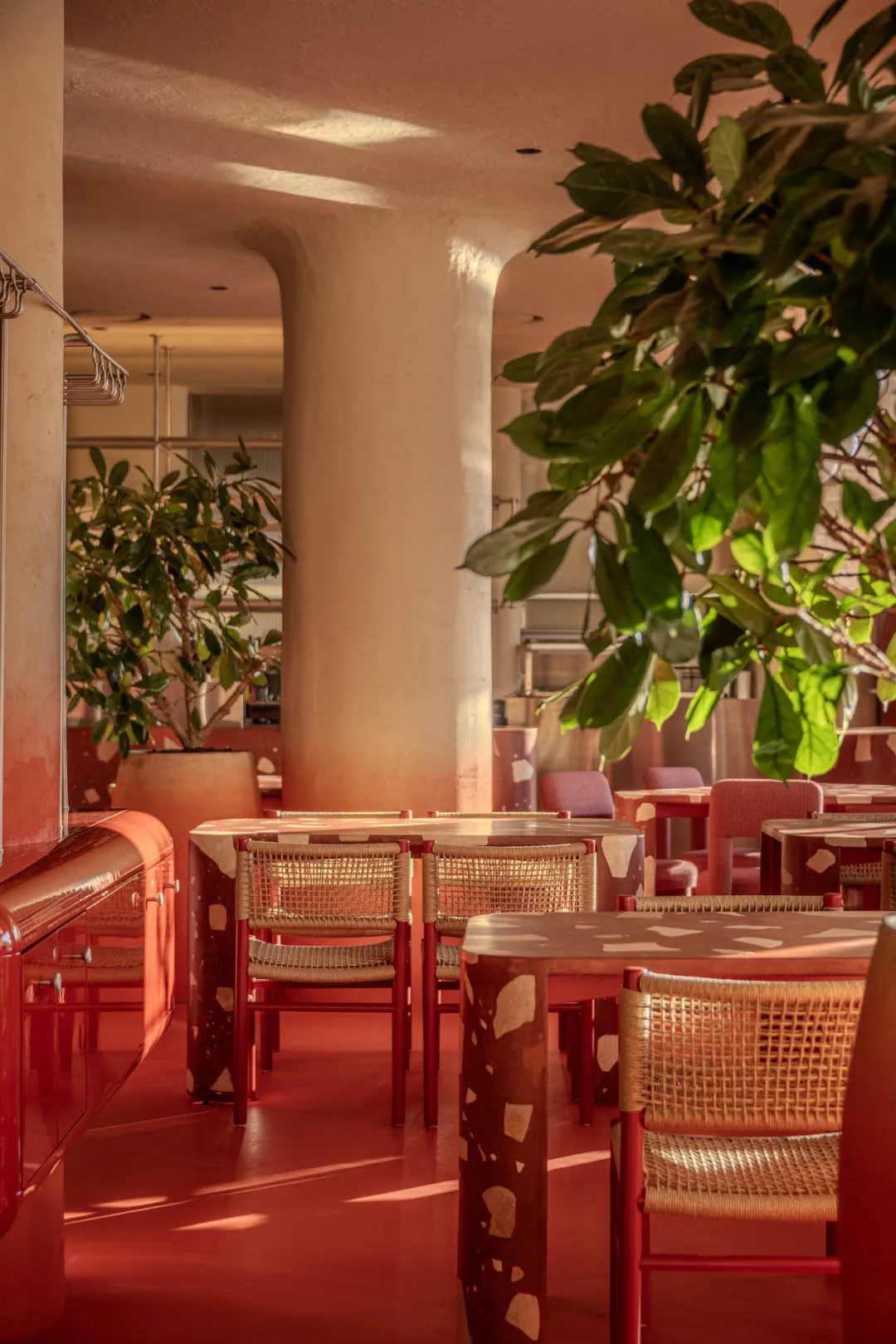 A modern restaurant interior with red tablecloths, red chairs, and large pillars, set in a well-lit dining area