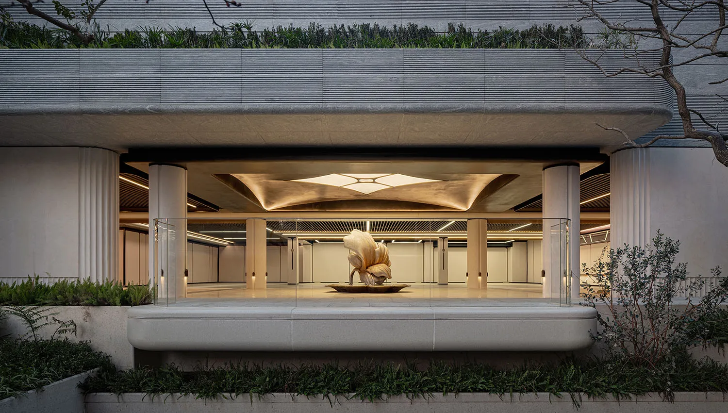 A dimly lit, modern building lobby with a large metal sculpture as the centerpiece, surrounded by concrete walls and floors