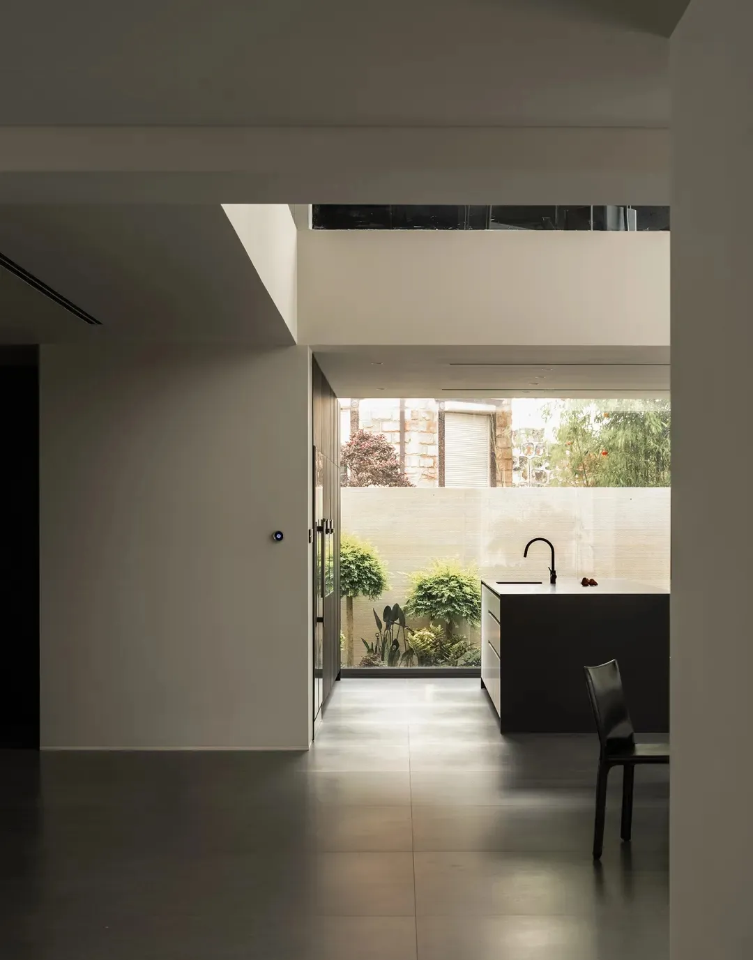 A modern kitchen with a white color scheme, featuring a sink, dining table, and chair, with natural light from a window creating a warm atmosphere