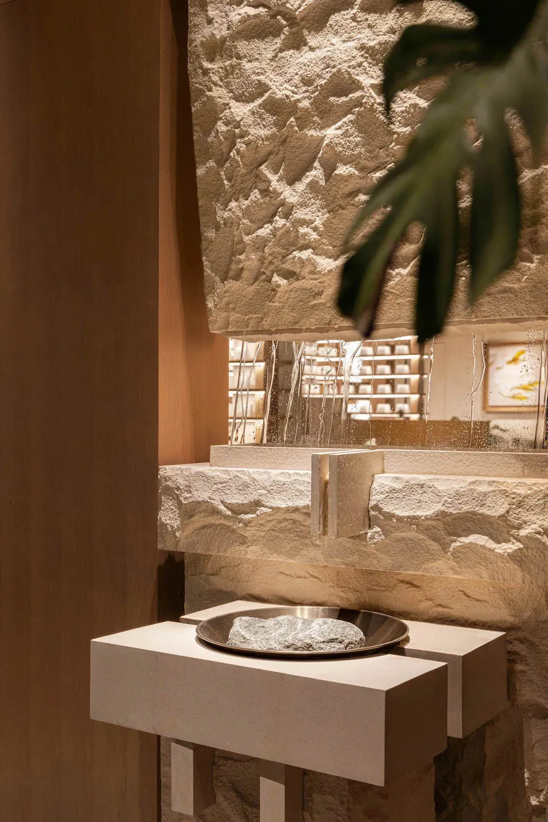 Bathroom with a stone wall, metal sink, and a potted plant, featuring dim lighting and a cozy atmosphere
