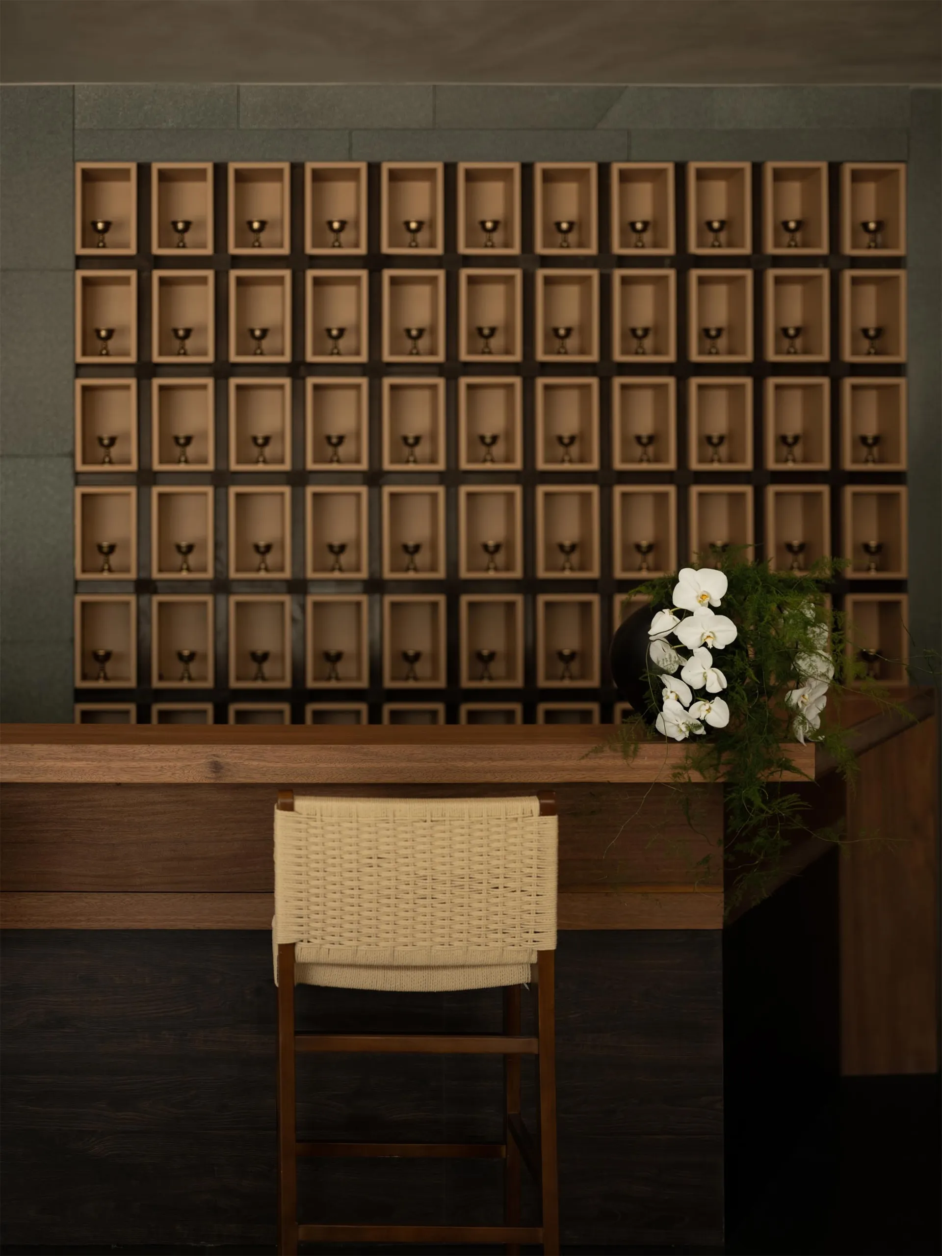 A warm and inviting hotel lobby with a wooden desk, chair, and decorative wine glasses, set against a neutral background