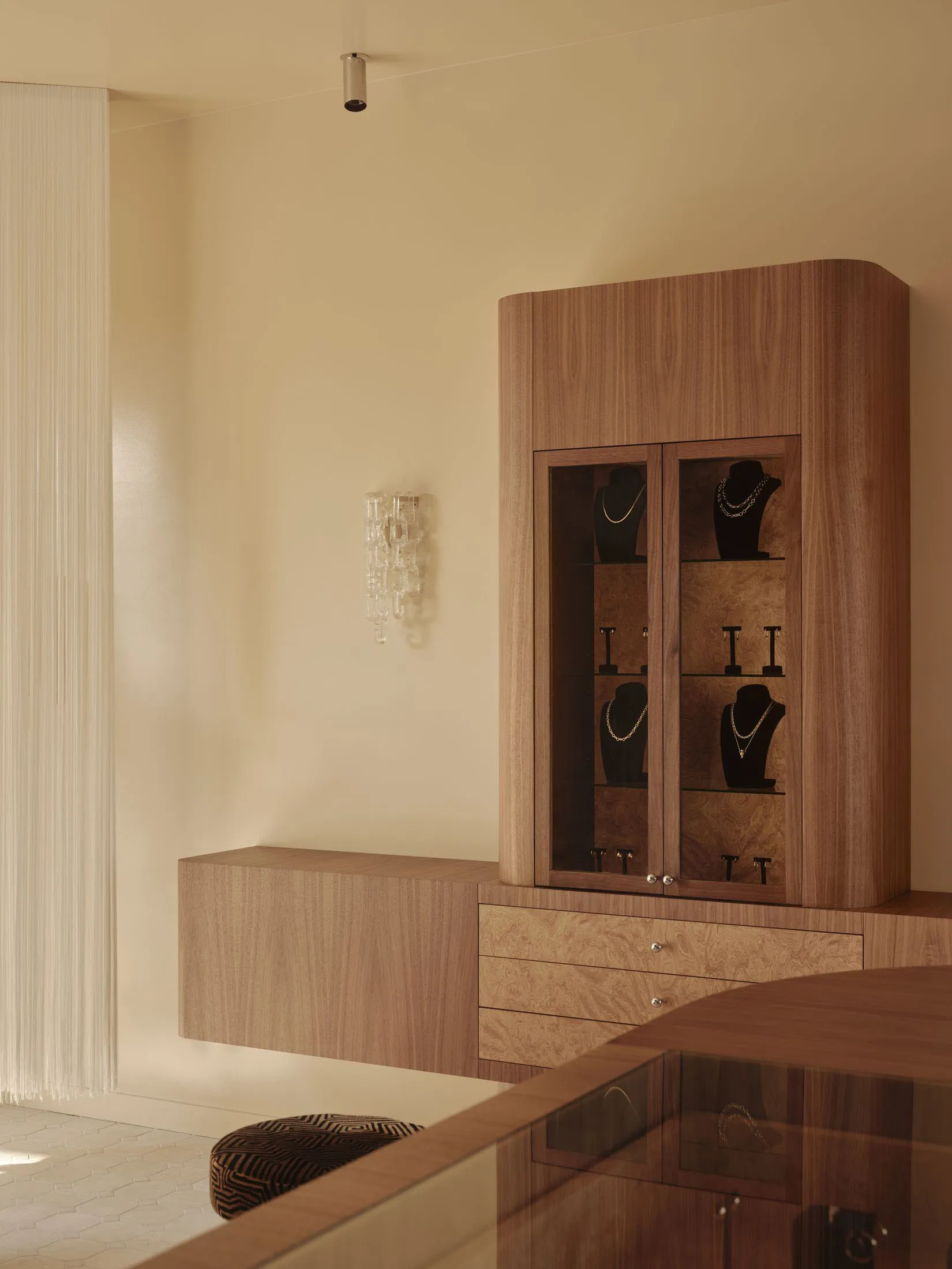 A dressing room with a wooden cabinet, soft warm lighting, and multiple necklaces hanging from it, creating a cozy atmosphere