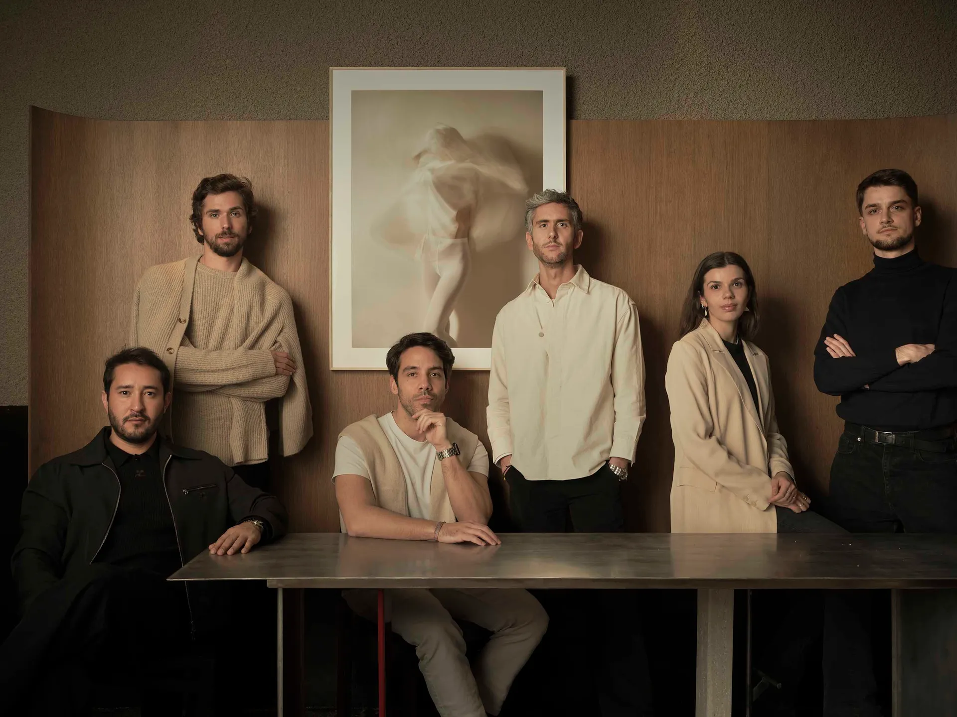 A group of people posing together in a casual gathering space with a dining table at its center, surrounded by natural and artificial lighting