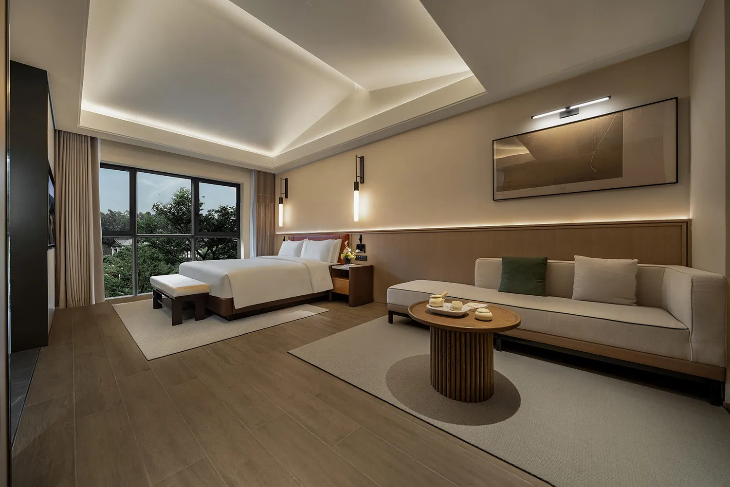 A well-lit bedroom with a wooden floor, a bed near a large window, and a couch in the opposite corner, creating a cozy atmosphere