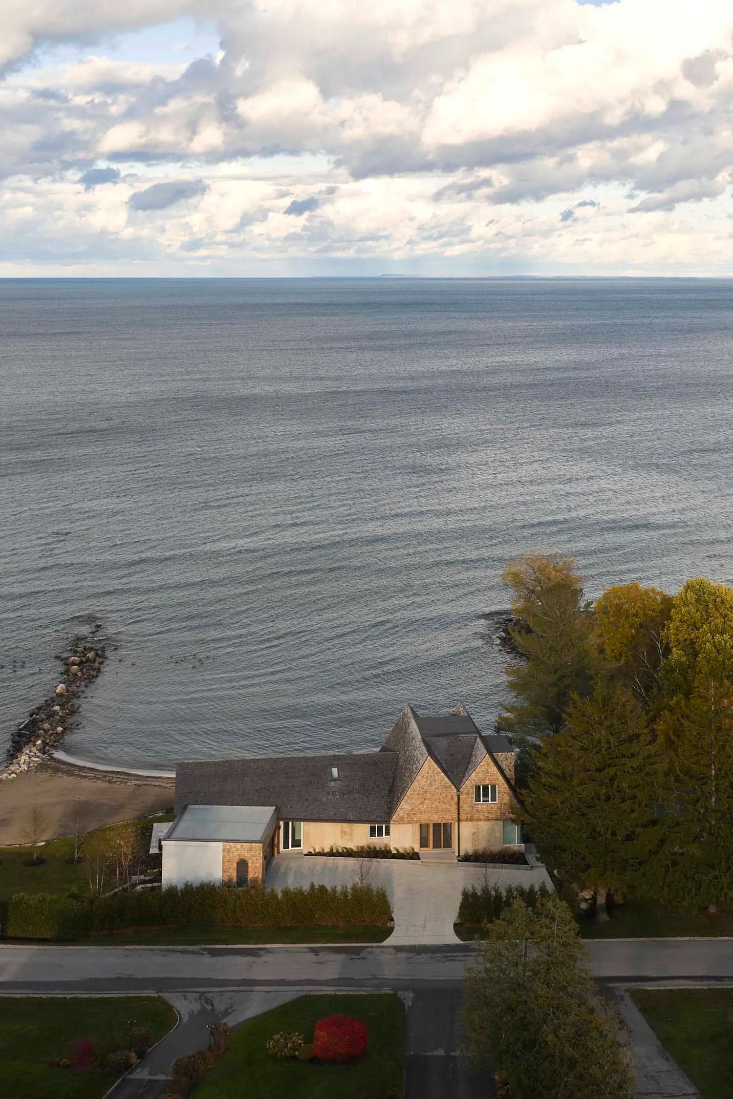A modern beach house with a large window on the second floor, surrounded by trees and natural scenery, bathed in natural light