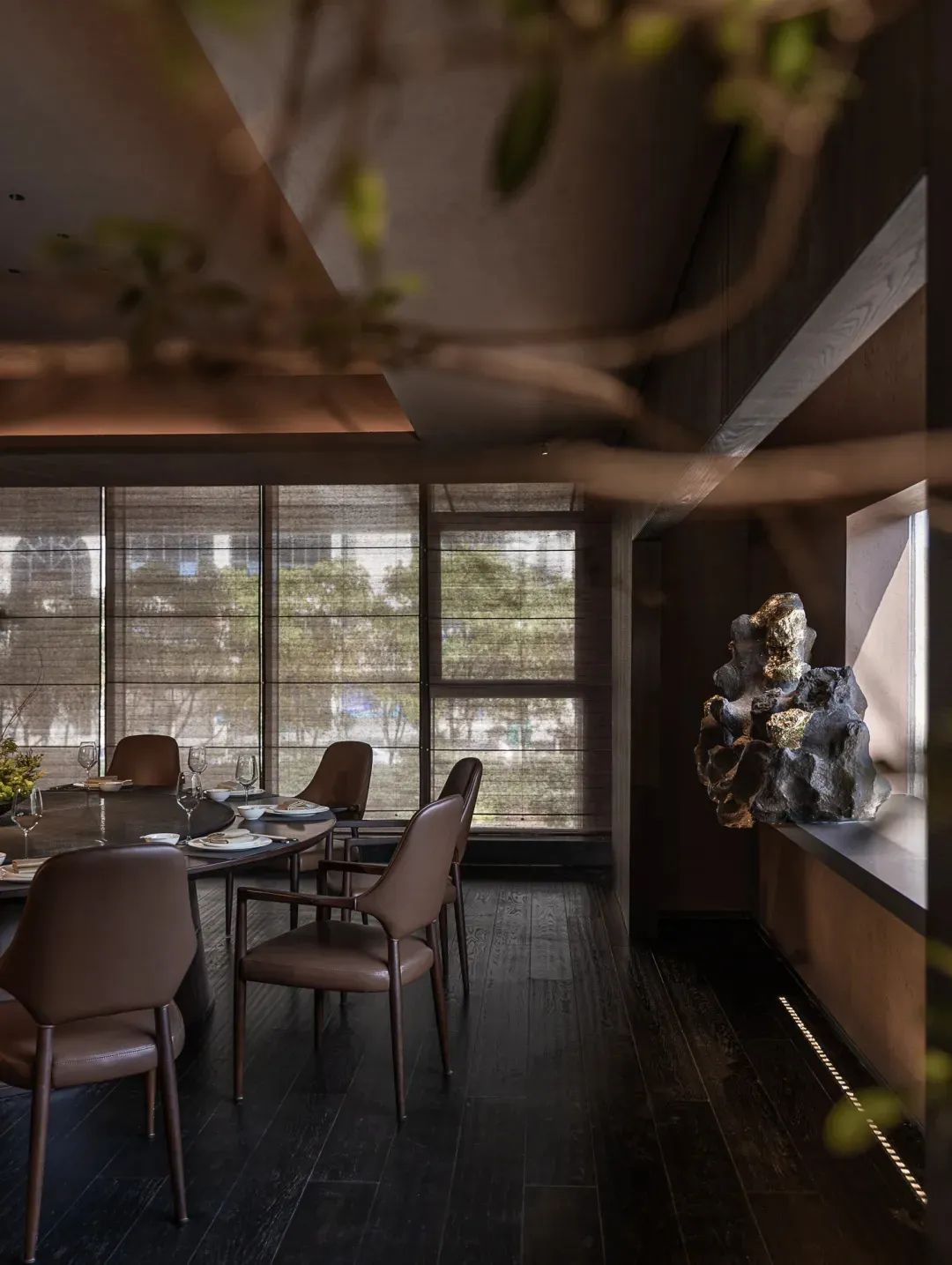Dining room with a large window, modern dining table, chairs, wine glasses, potted plant, and vase, lit by natural light