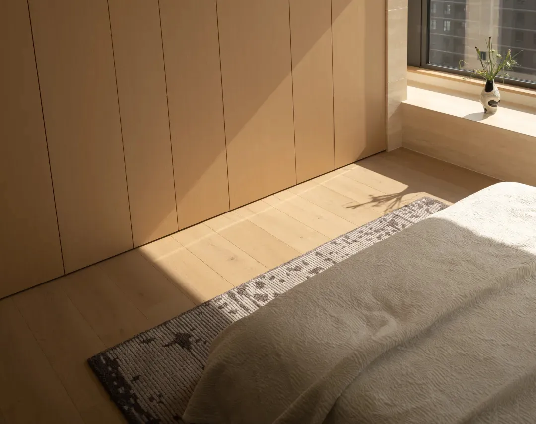 Cozy bedroom with a bed on a wooden floor, a wooden door, and a window in the background, well-lit and inviting