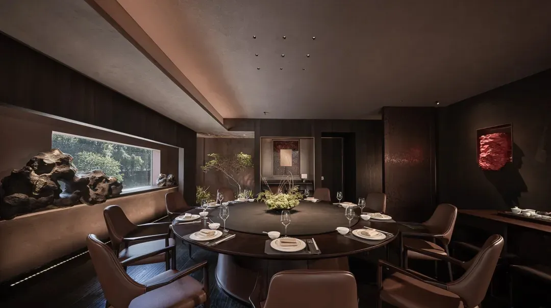 A dimly lit dining room with a round table set for a meal, surrounded by black chairs in a brown room