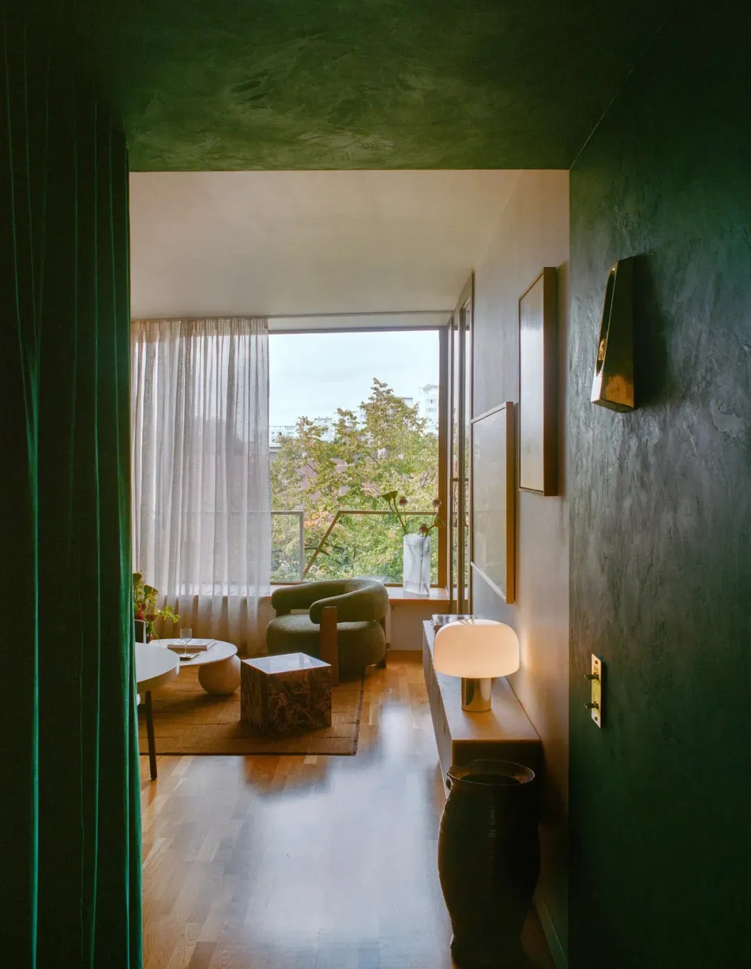 A well-lit living room with a green color scheme, featuring a couch, chair, dining table, and potted plant, creating a cozy and inviting atmosphere