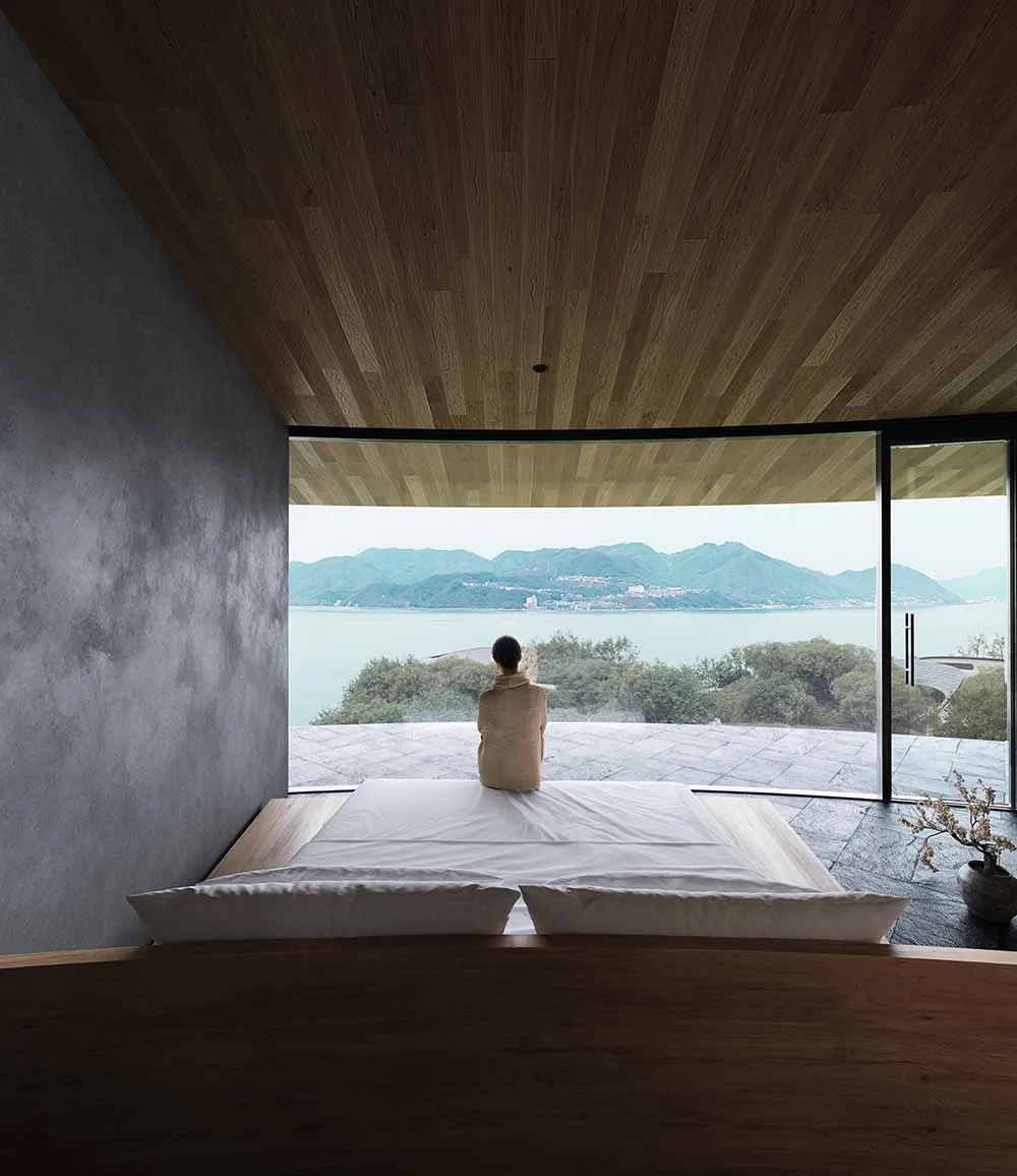 Serene bedroom with a large window offering an ocean view, a wooden headboard, and a white bed sheet in a well-lit space