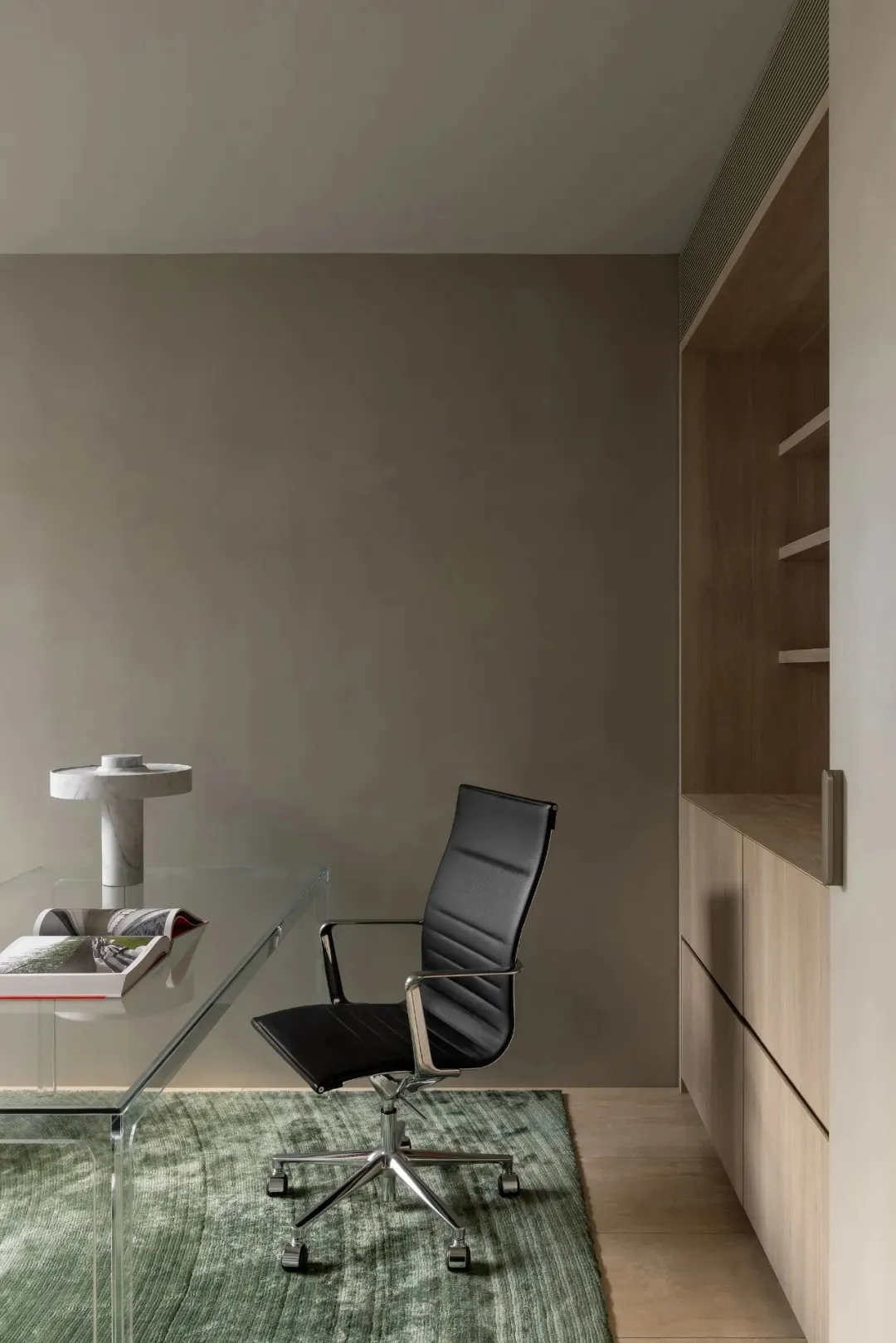A dimly lit room with a glass table and a black chair, surrounded by a modern and minimalist space with a wall and door in the background