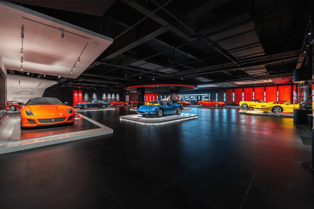 Black and white photograph of a modern sports car showroom with various sports cars on display, including a blue and red car, in an elegant and sophisticated setting