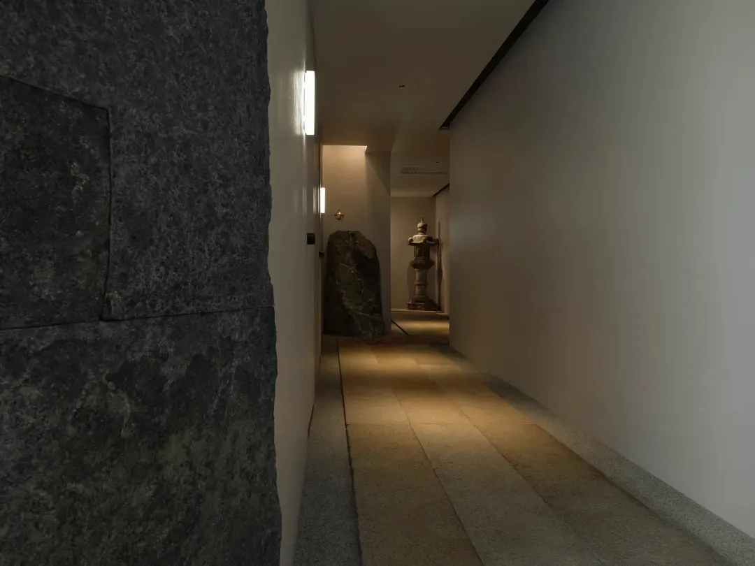 A dimly lit hallway with stone walls, featuring a statue on display, creating a mysterious atmosphere reminiscent of a museum or historical building