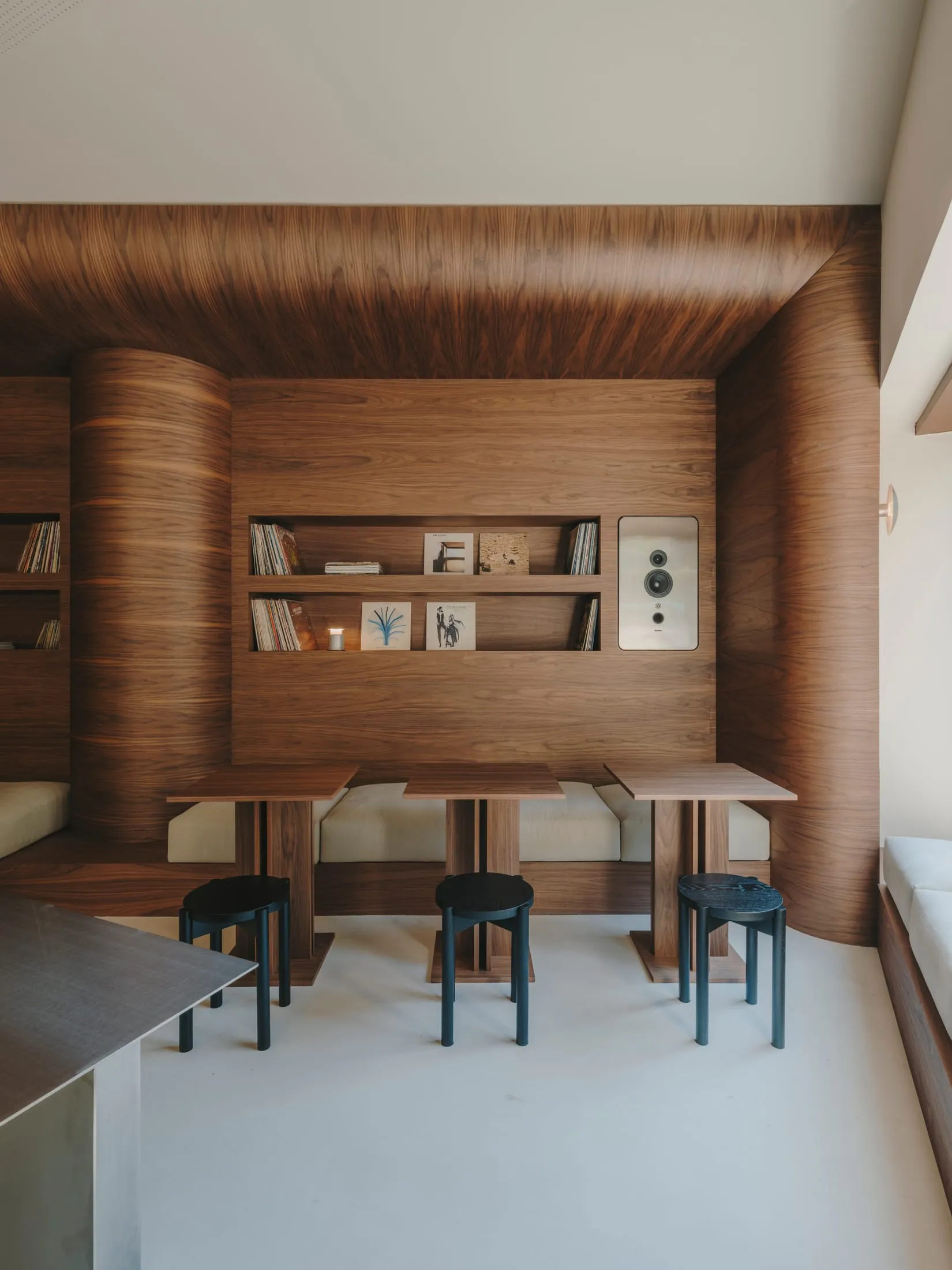 Warm and cozy living space with wooden walls and floors, a dining table, bookshelf, and couch, well-lit with natural light from windows