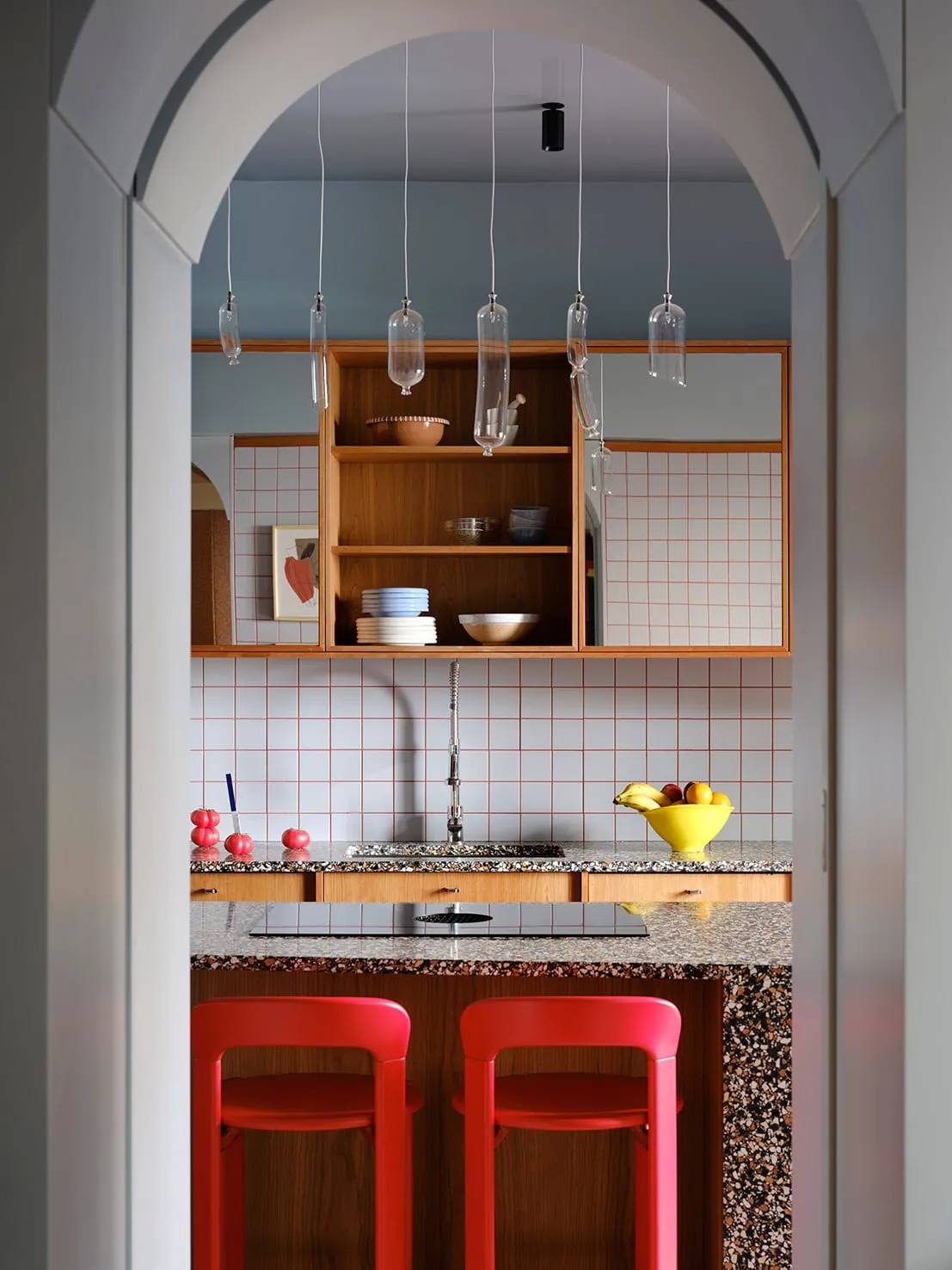 A cozy kitchen with a granite countertop, stainless steel sink, and a dining table with a red and yellow chair, surrounded by bowls and cups, in a dimly lit space