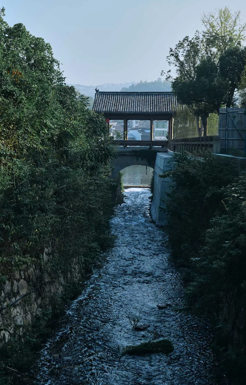 一幅靜謐的河流景色，石橋和附近的小建築，設置在自然環境中