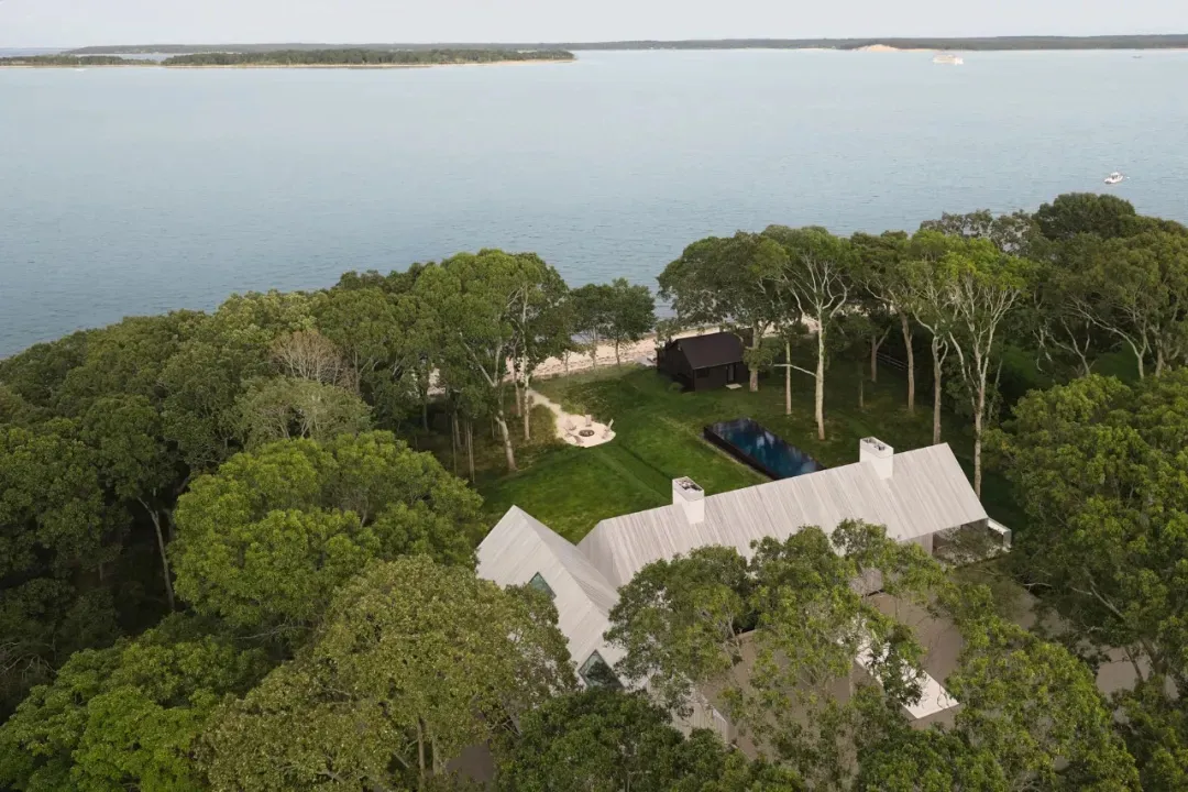 A modern house with a white exterior and black roof, surrounded by a pool and trees, with natural sunlight and a serene atmosphere