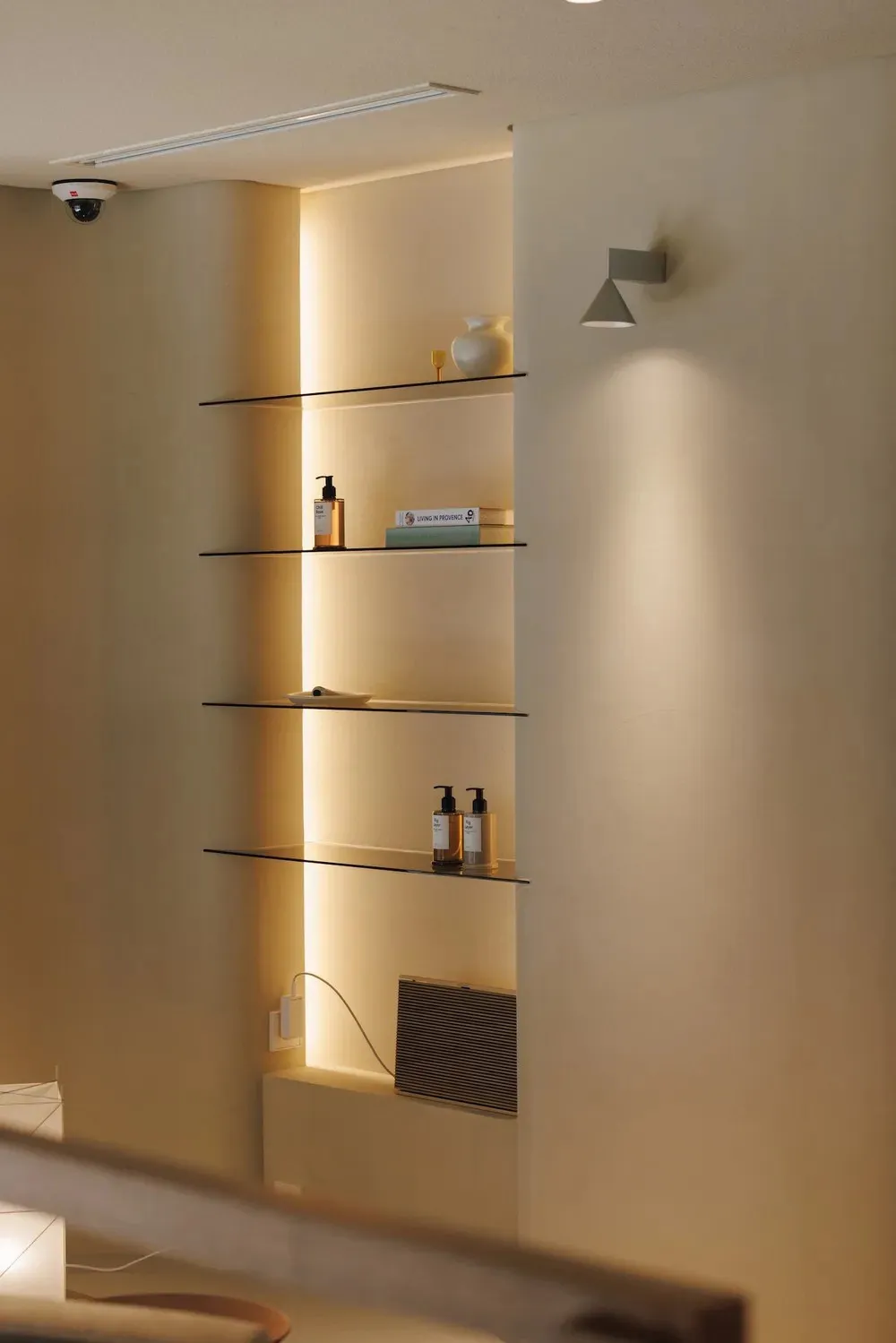 Bathroom with a shelf filled with bottles and a book, featuring a white color scheme and soft warm lighting