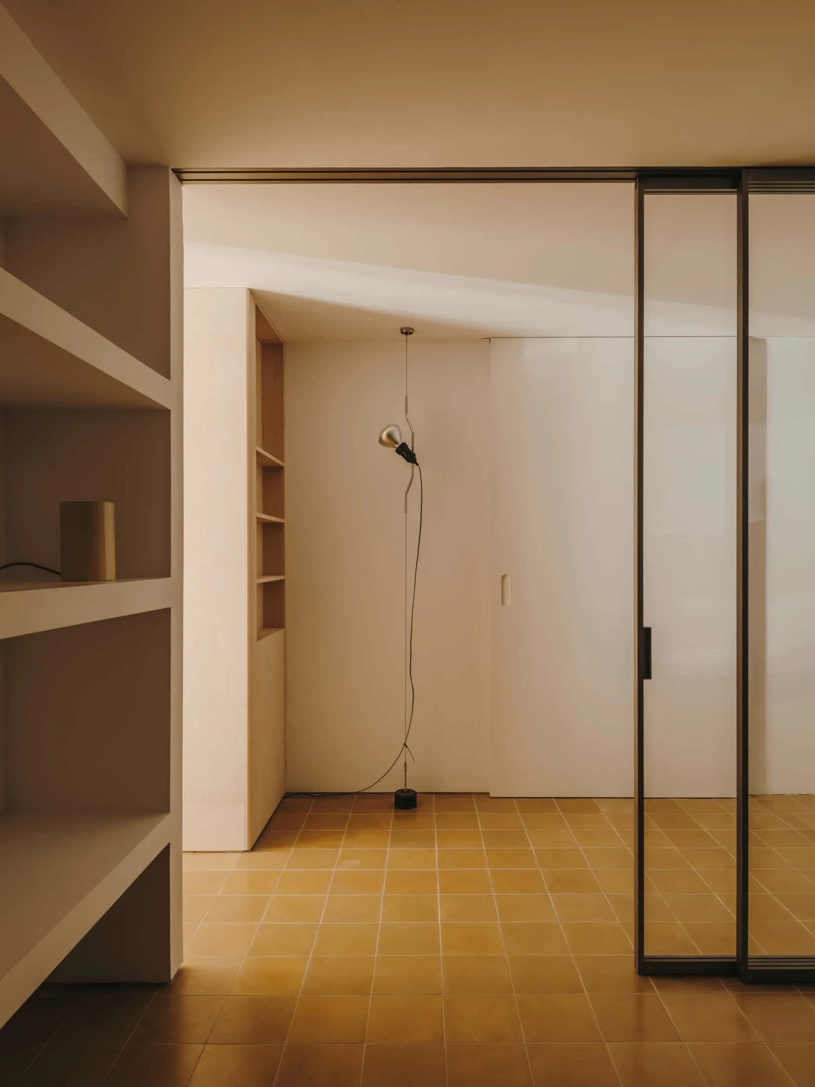 A small, dimly lit room with a yellow floor, white walls, and a doorway and window