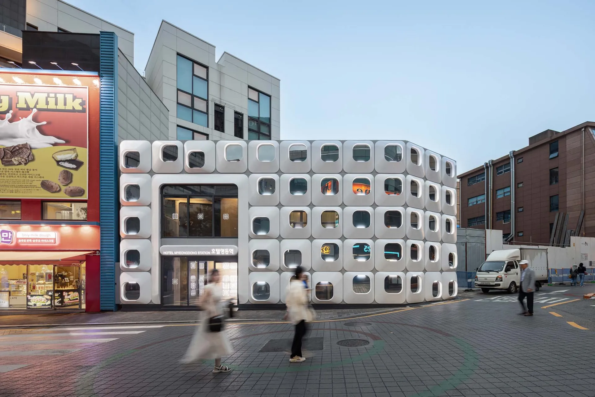 A modern building with a unique design featuring a large number of small white boxes arranged in a circular pattern, set against a well-lit background with natural light coming in from the windows