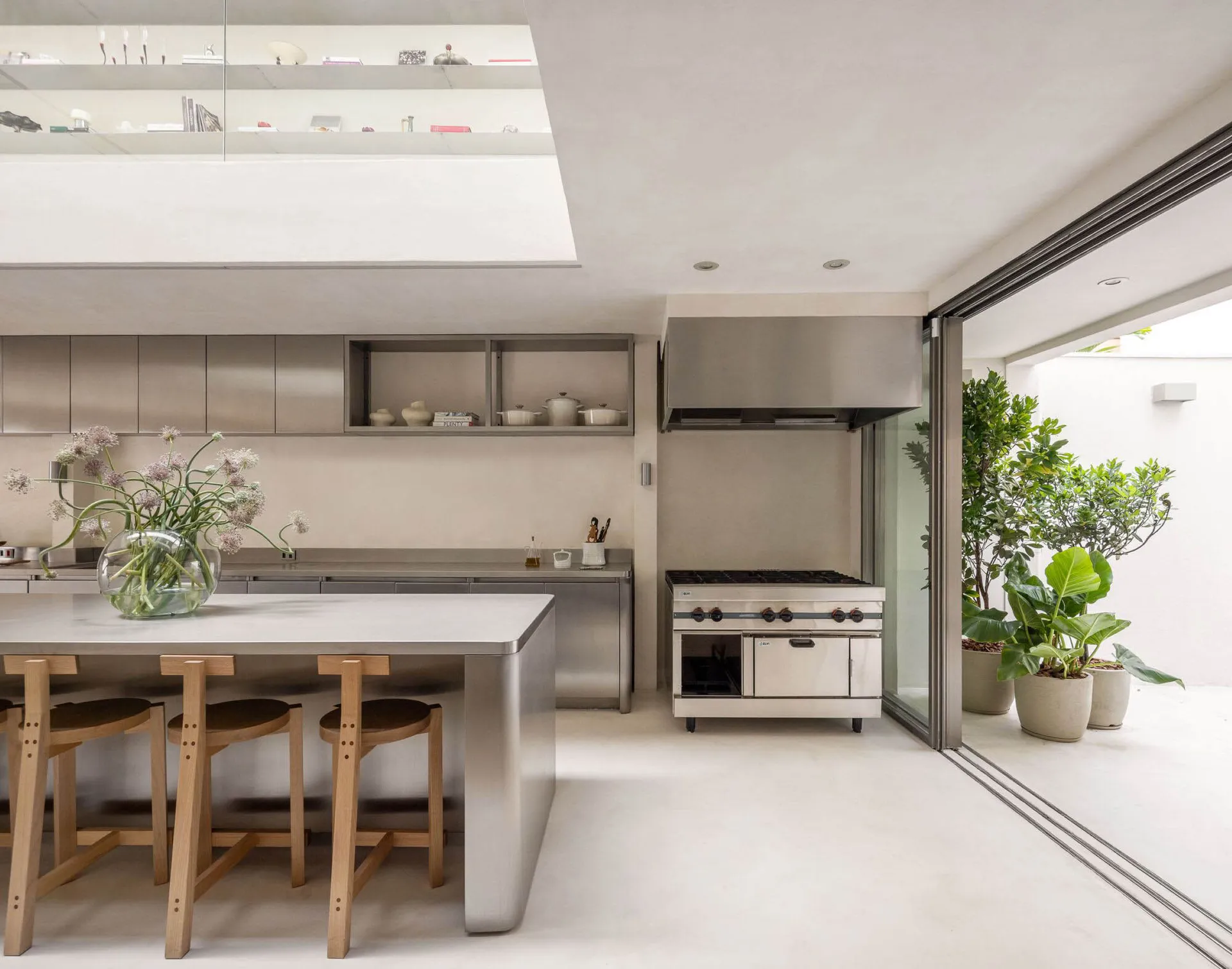 Well-lit modern kitchen with a large island, two dining tables, and various appliances, surrounded by white walls and a silver countertop