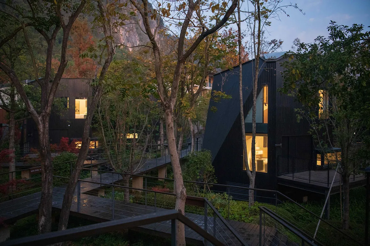 A black house with a modern design surrounded by trees, showcasing a well-lit and inviting interior through the windows
