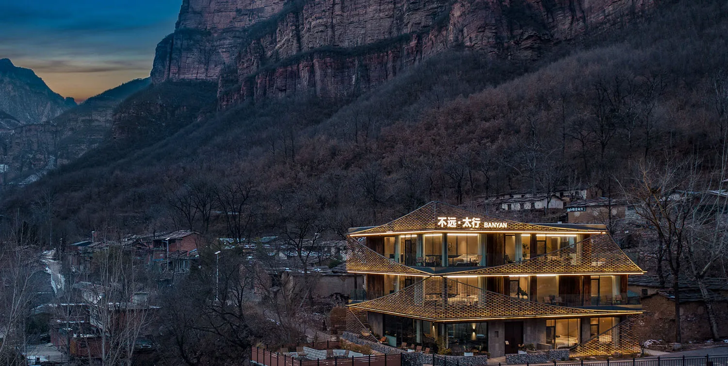 A modern hotel building with a yellow and brown exterior, situated in front of a mountain, with natural light and an inviting atmosphere