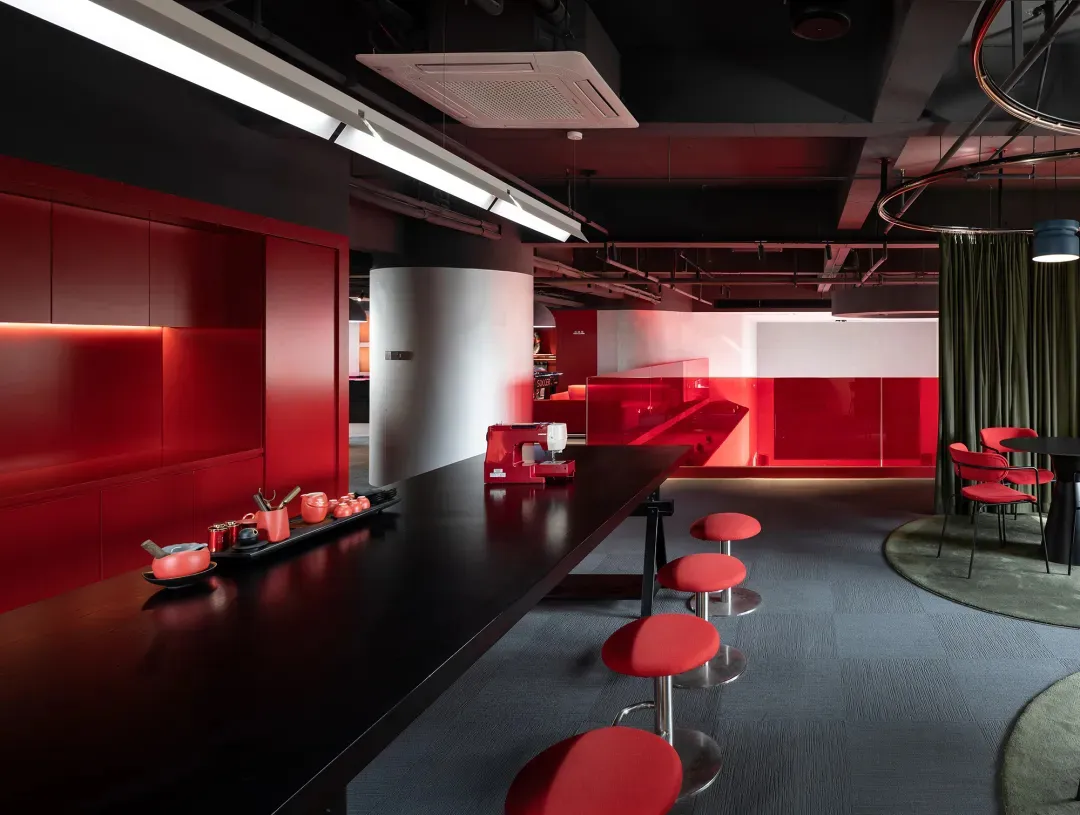 A modern dining space with red walls, a black table, and red chairs, well-lit with natural light from a window