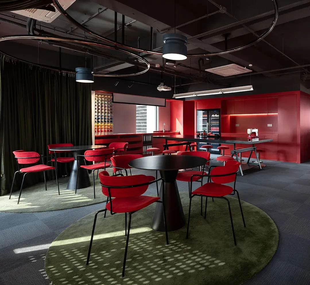 A modern dining space with a red and black color scheme, featuring a dining table and chairs, a kitchen area with a refrigerator and sink, and dim lighting creating a warm and intimate ambiance