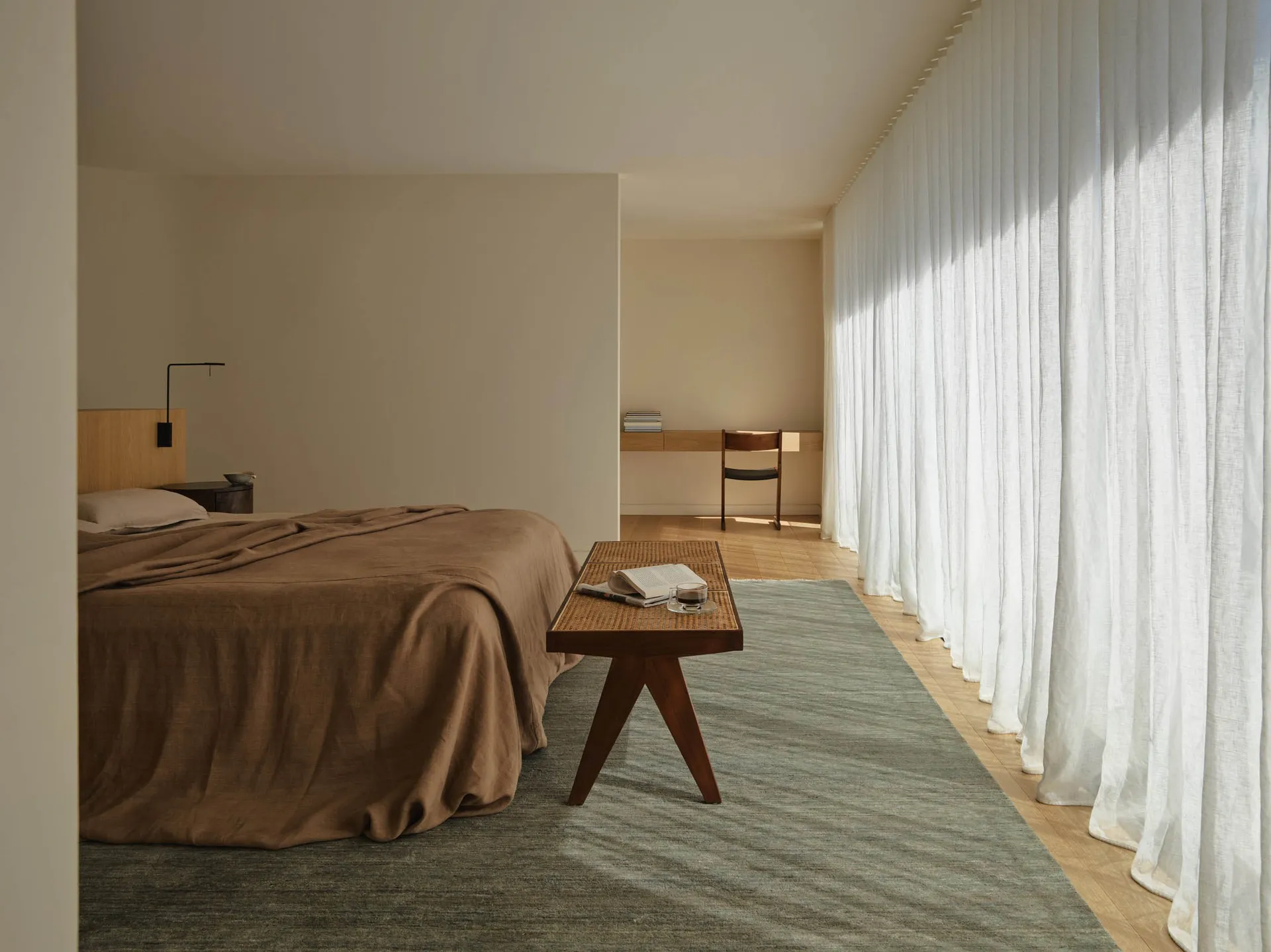 Cozy bedroom with a brown blanket-covered bed, a wooden chair, and a wooden table, set in a well-lit room with a warm atmosphere